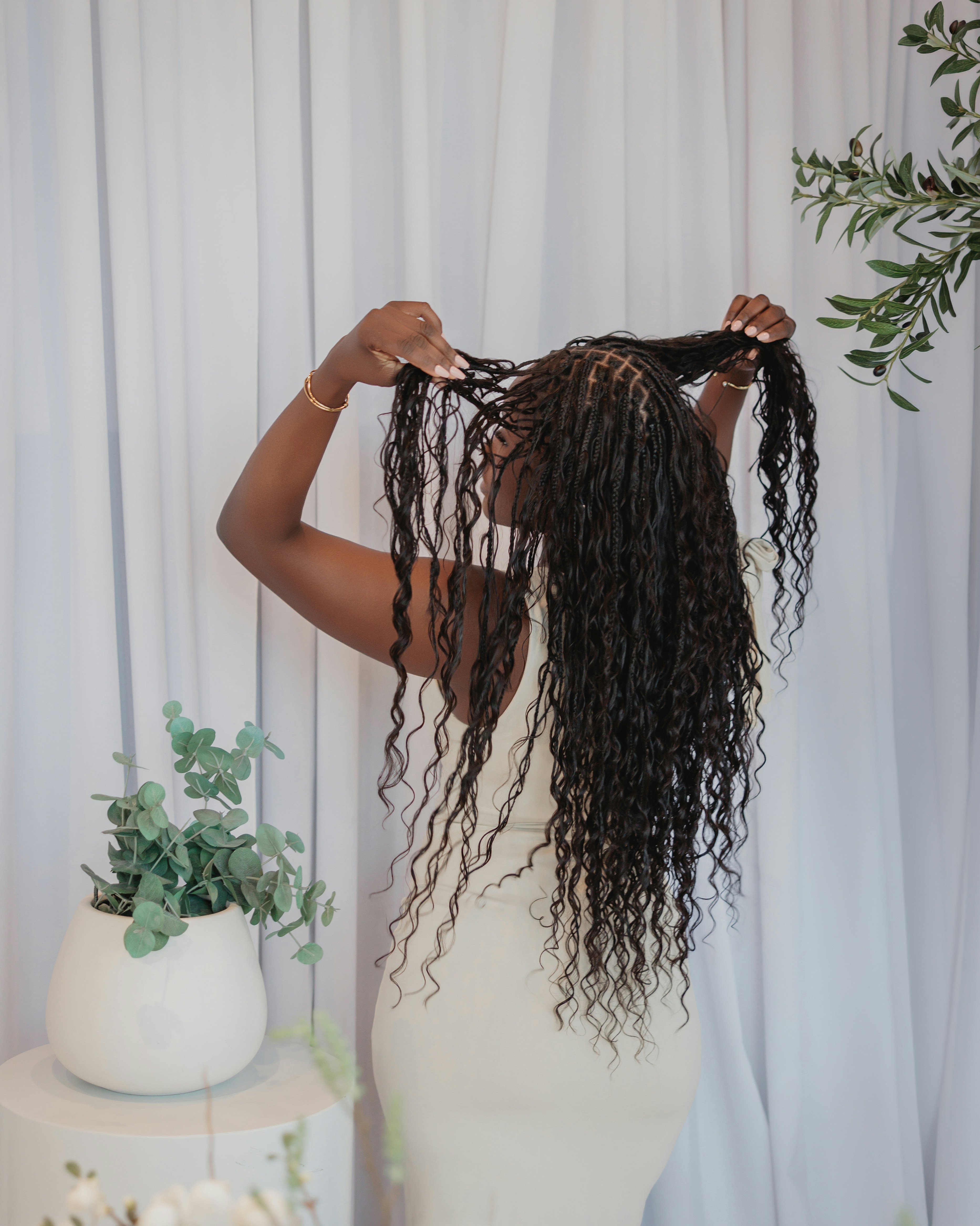 Woman holding up a section of long braids in front of a white curtain