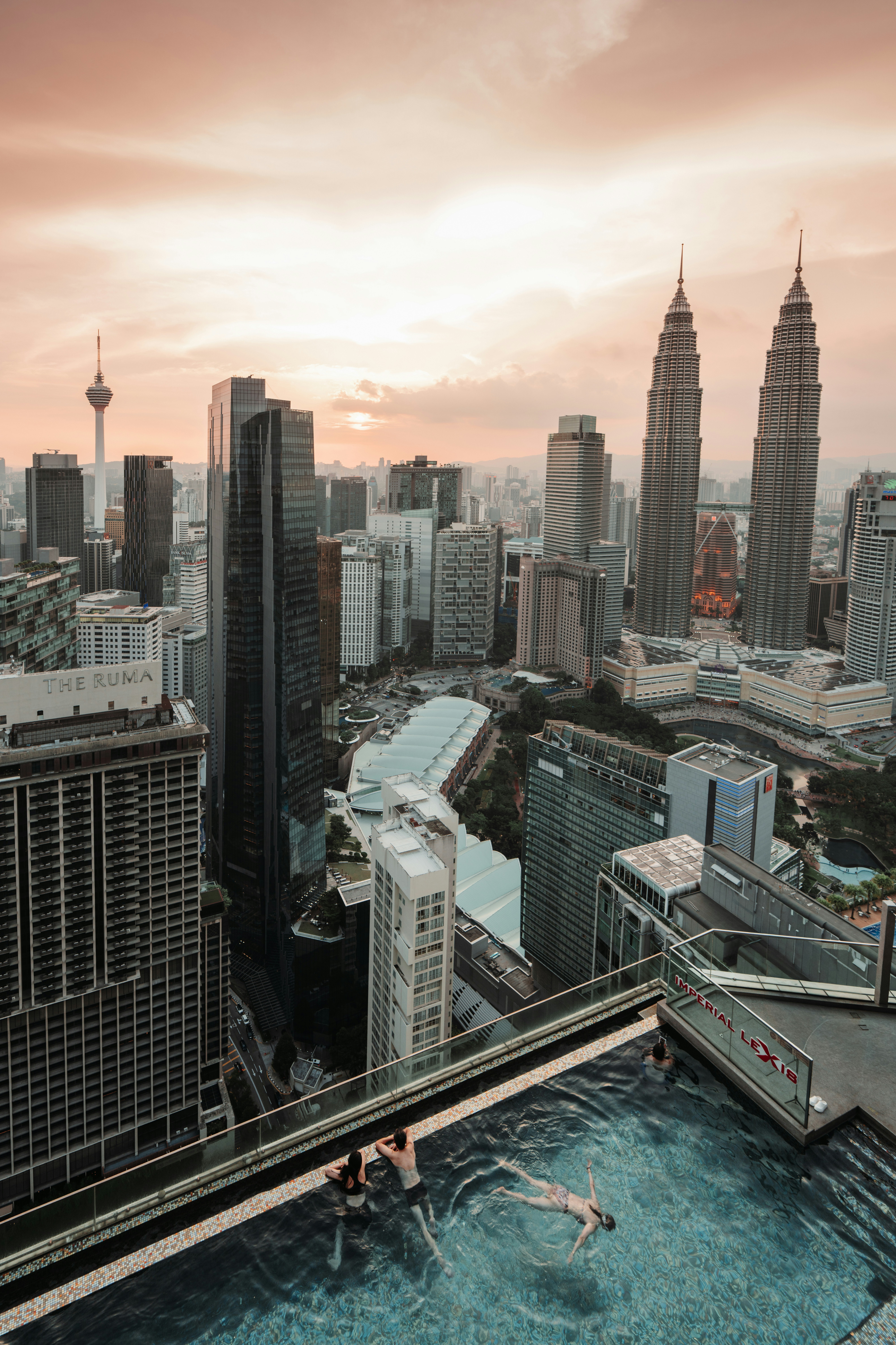 Swimmers in rooftop pool overlooking kuala lumpur at sunset
