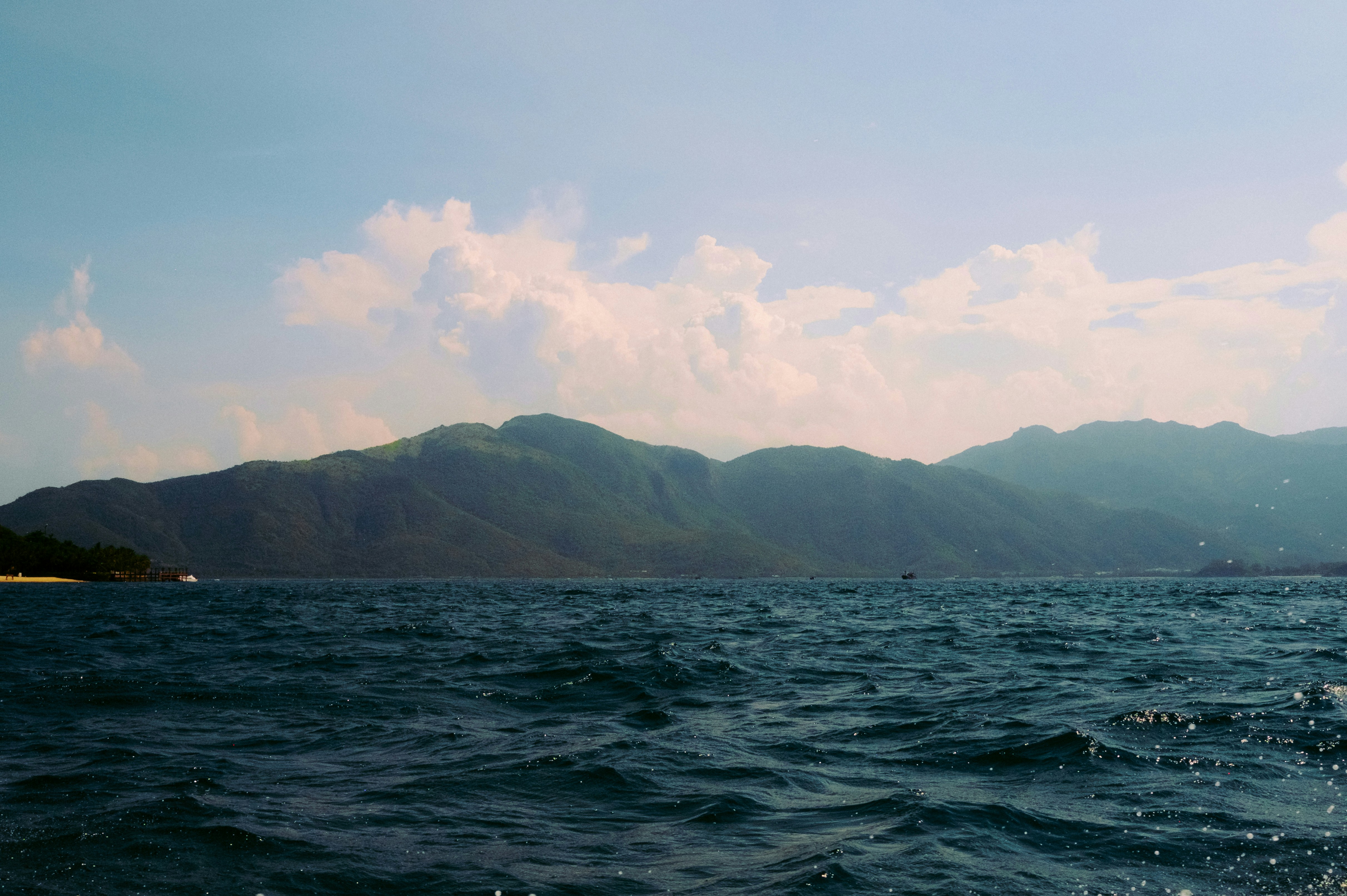 Olas azules del océano con montañas verdes bajo un cielo nublado.