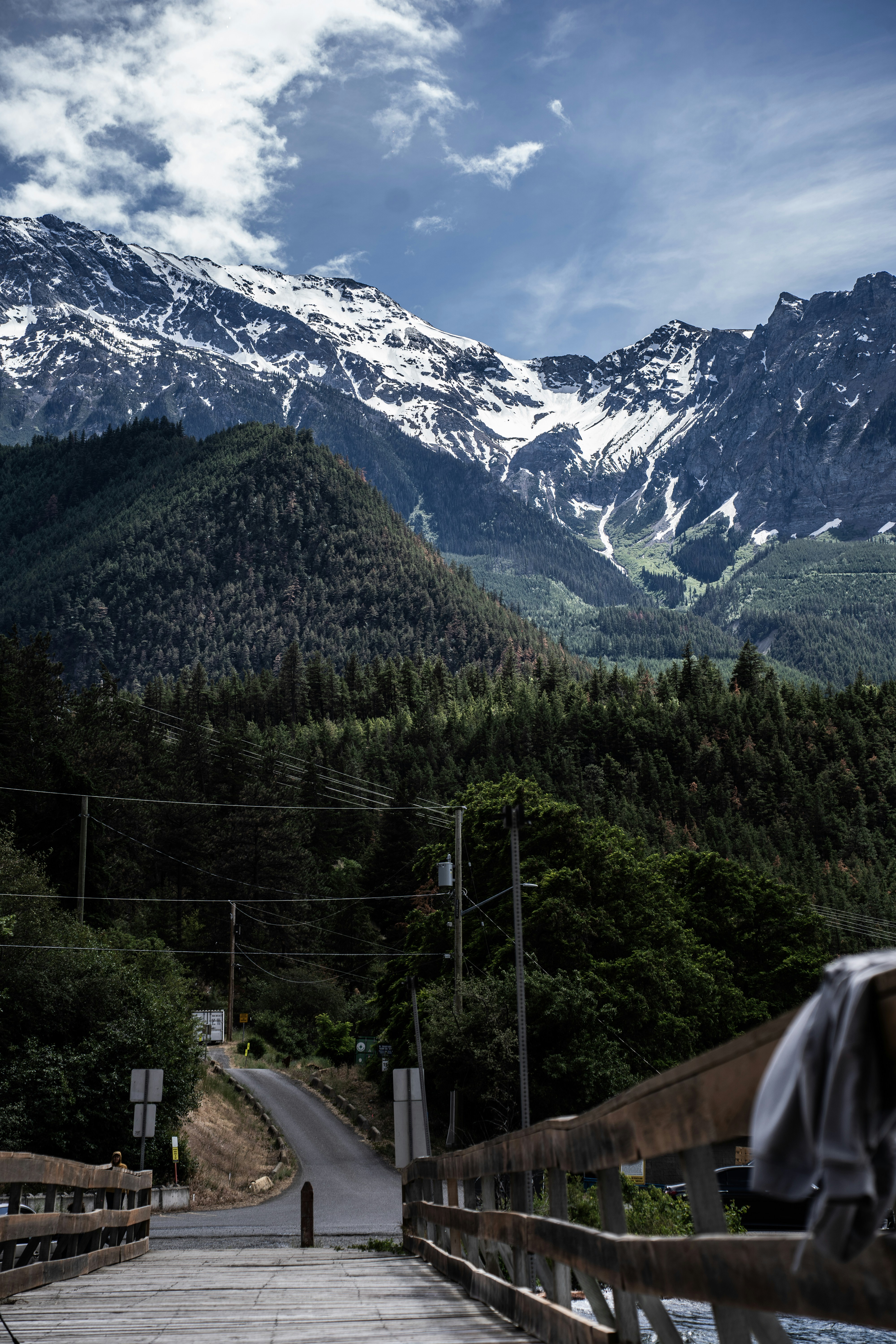 Majestuosas montañas nevadas se alzan sobre un bosque y un puente.