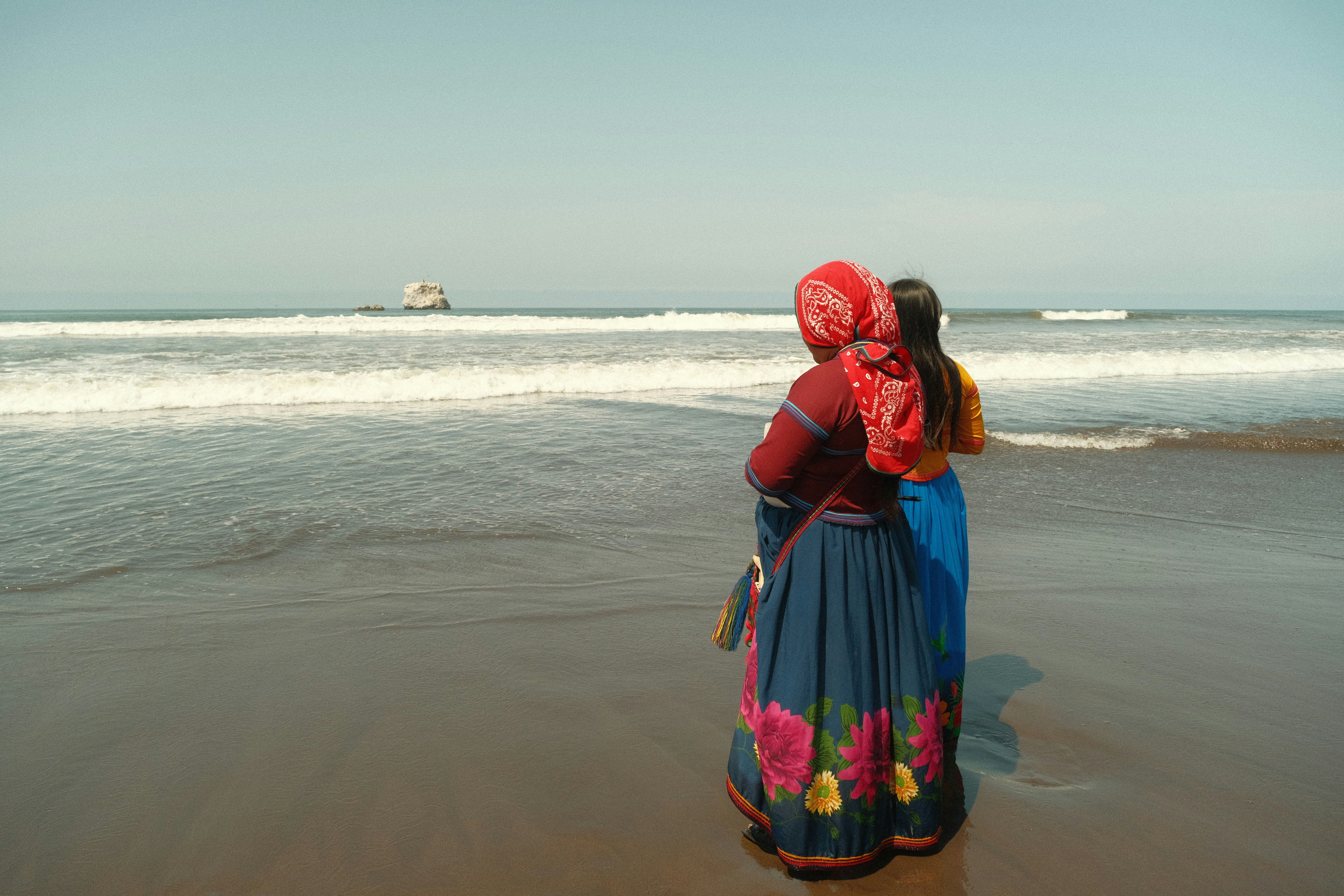 Two women watch ocean waves from a sandy beach