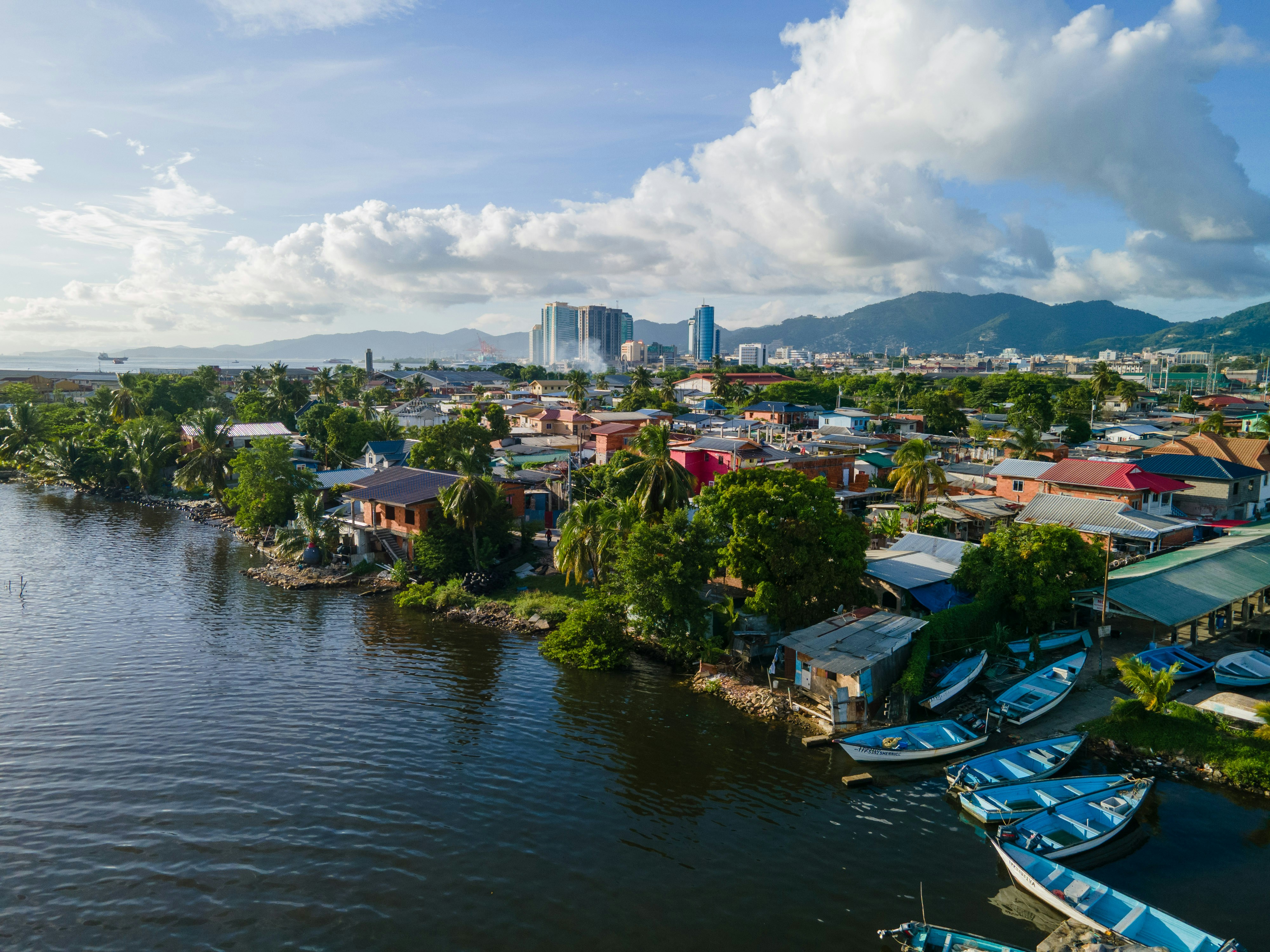 Boats along a river with a town and city skyline.