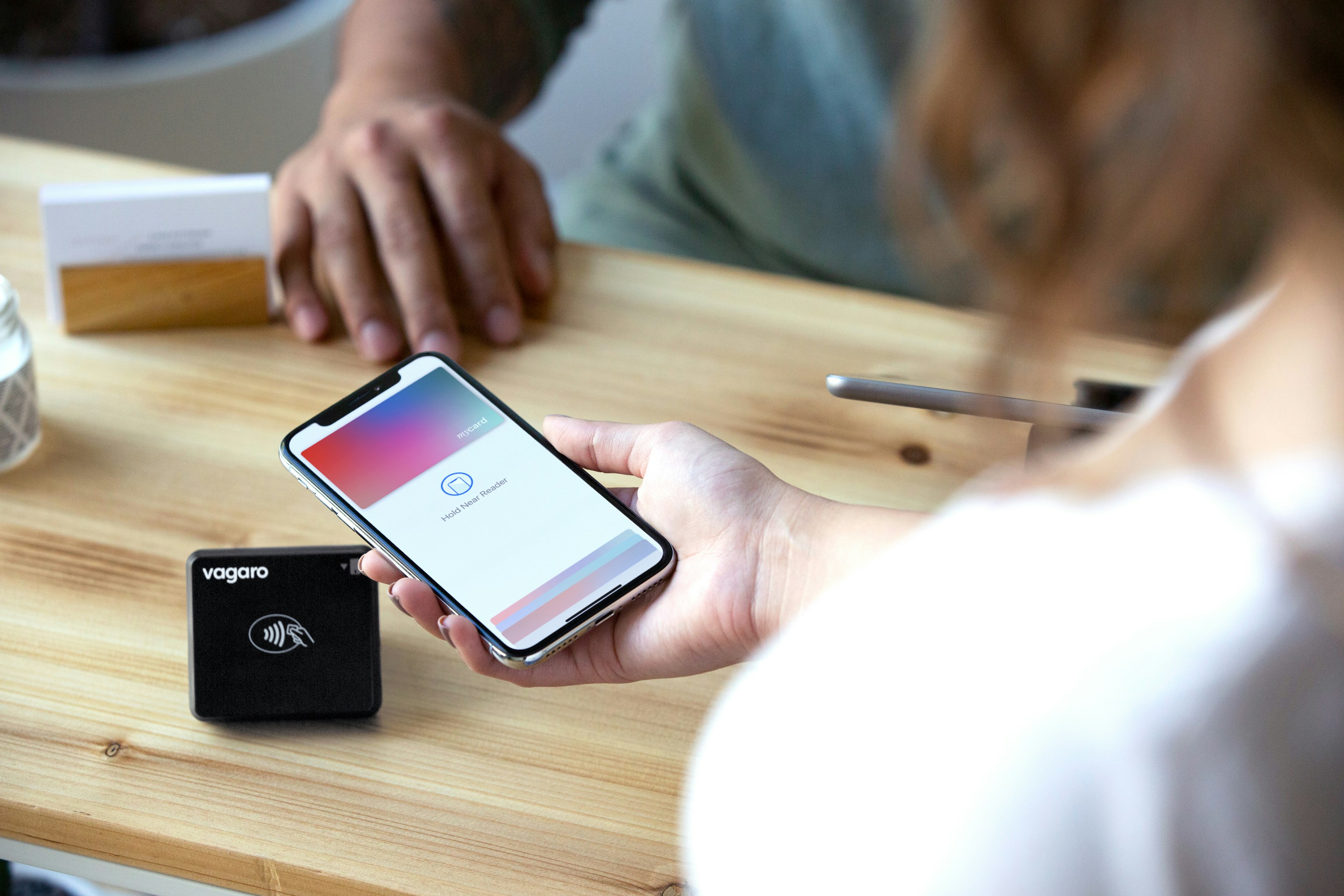 Woman holds smartphone near card reader for transaction.