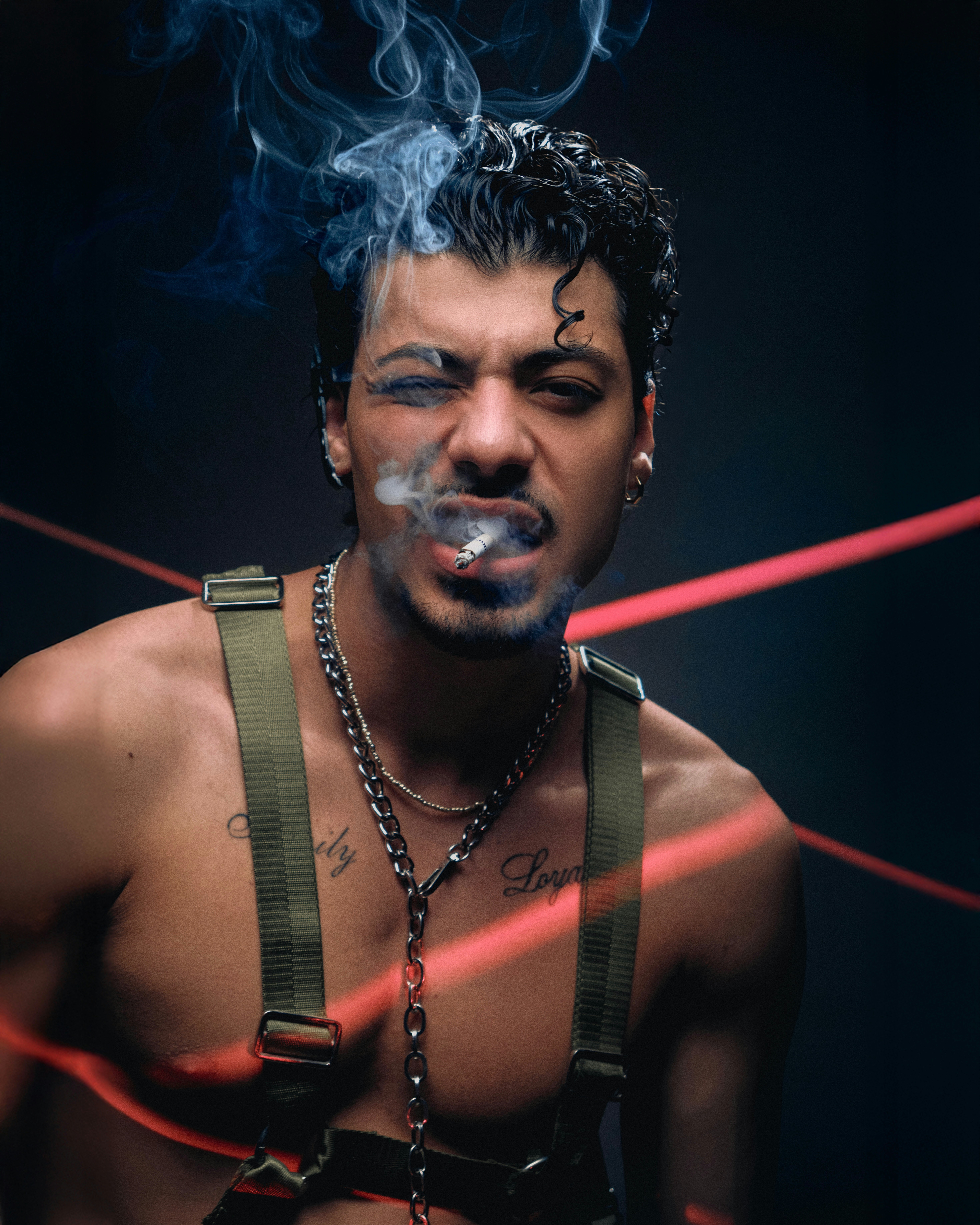 Uomo intenso che fuma una sigaretta con catene e laser rossi.
