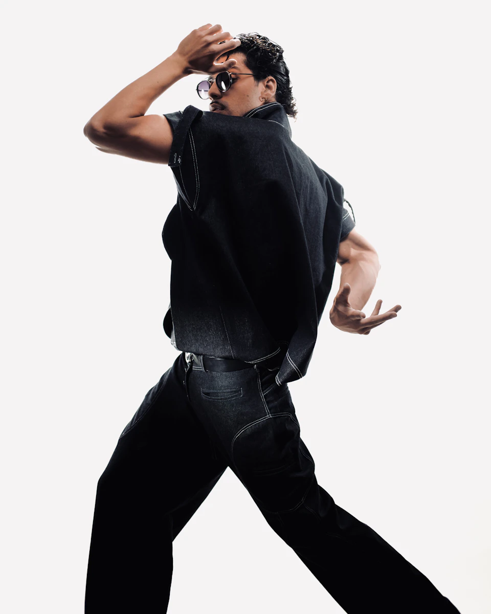 Model mid-stride in a black denim vest and wide black trousers, studio white background