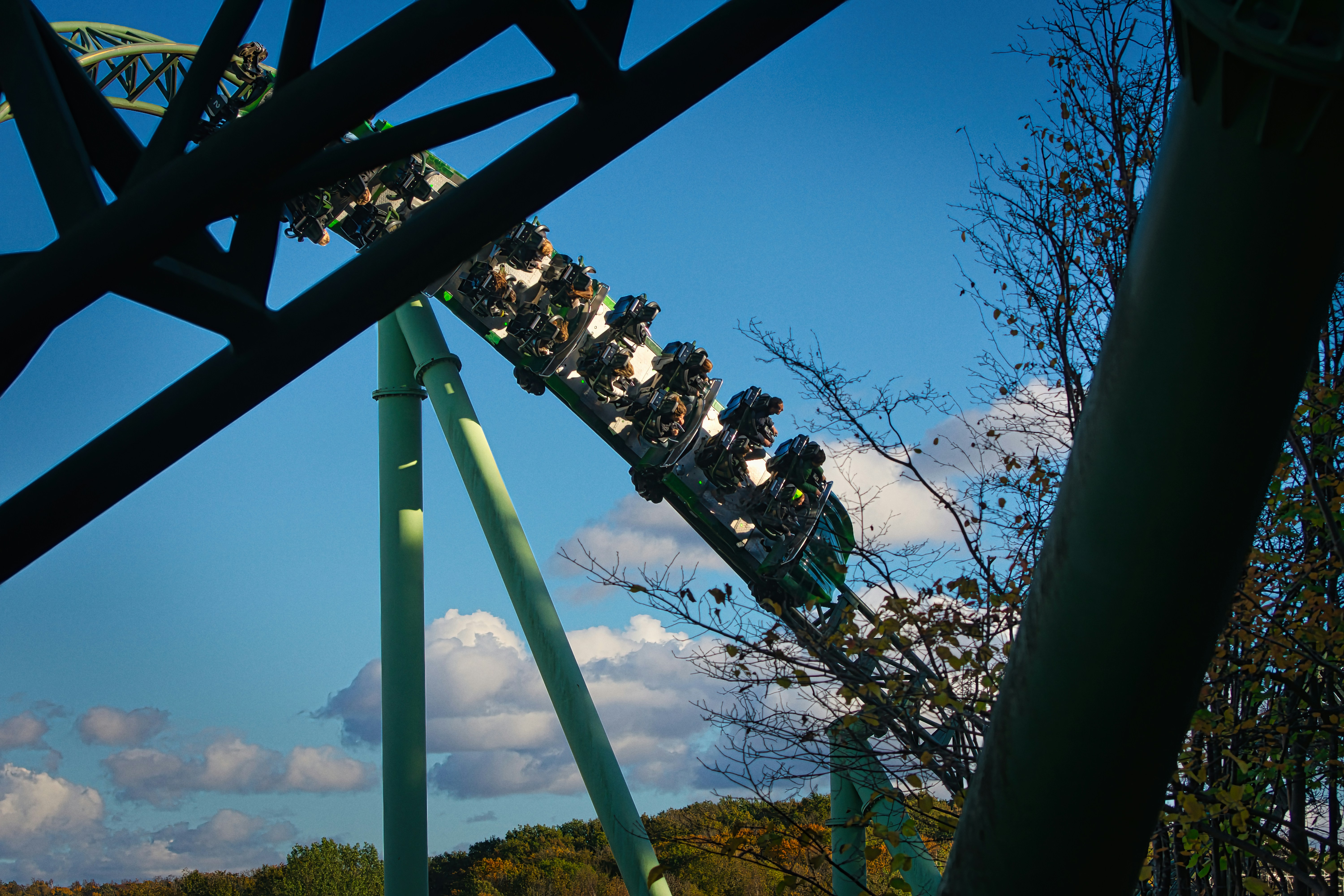 Green roller coaster with riders against a blue sky.