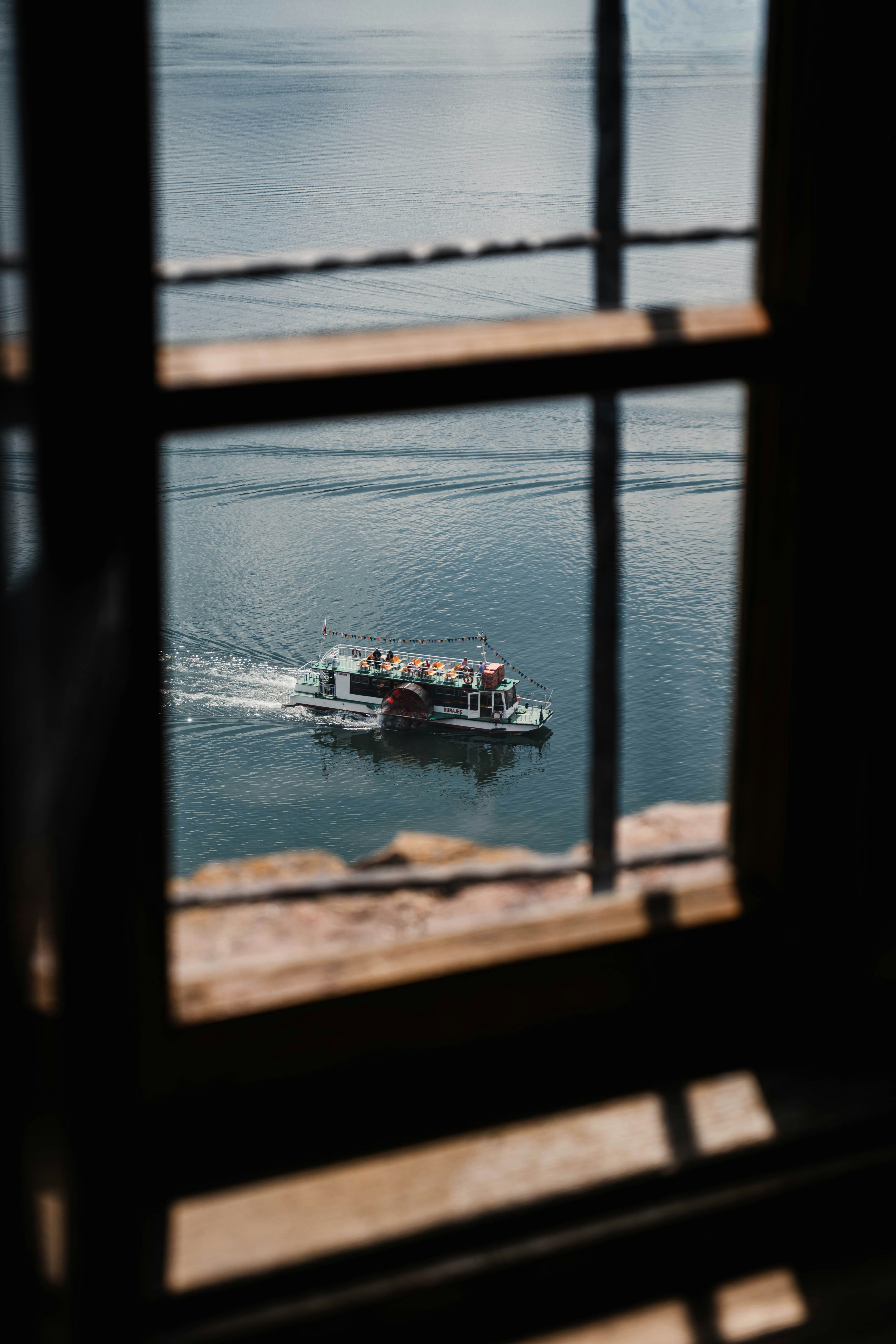 A boat moves across water, framed by a dark window.