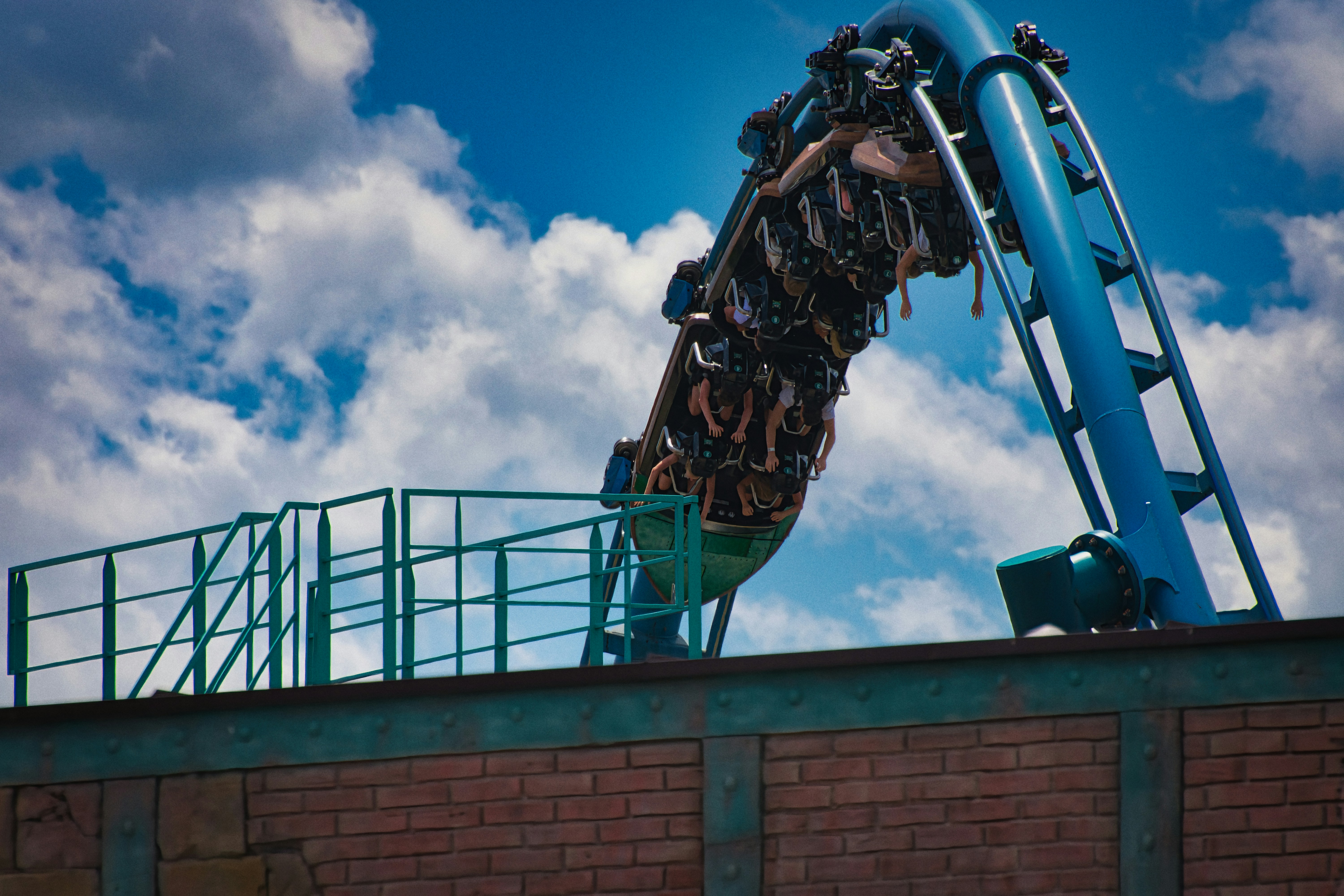 People riding a blue roller coaster against a cloudy sky.