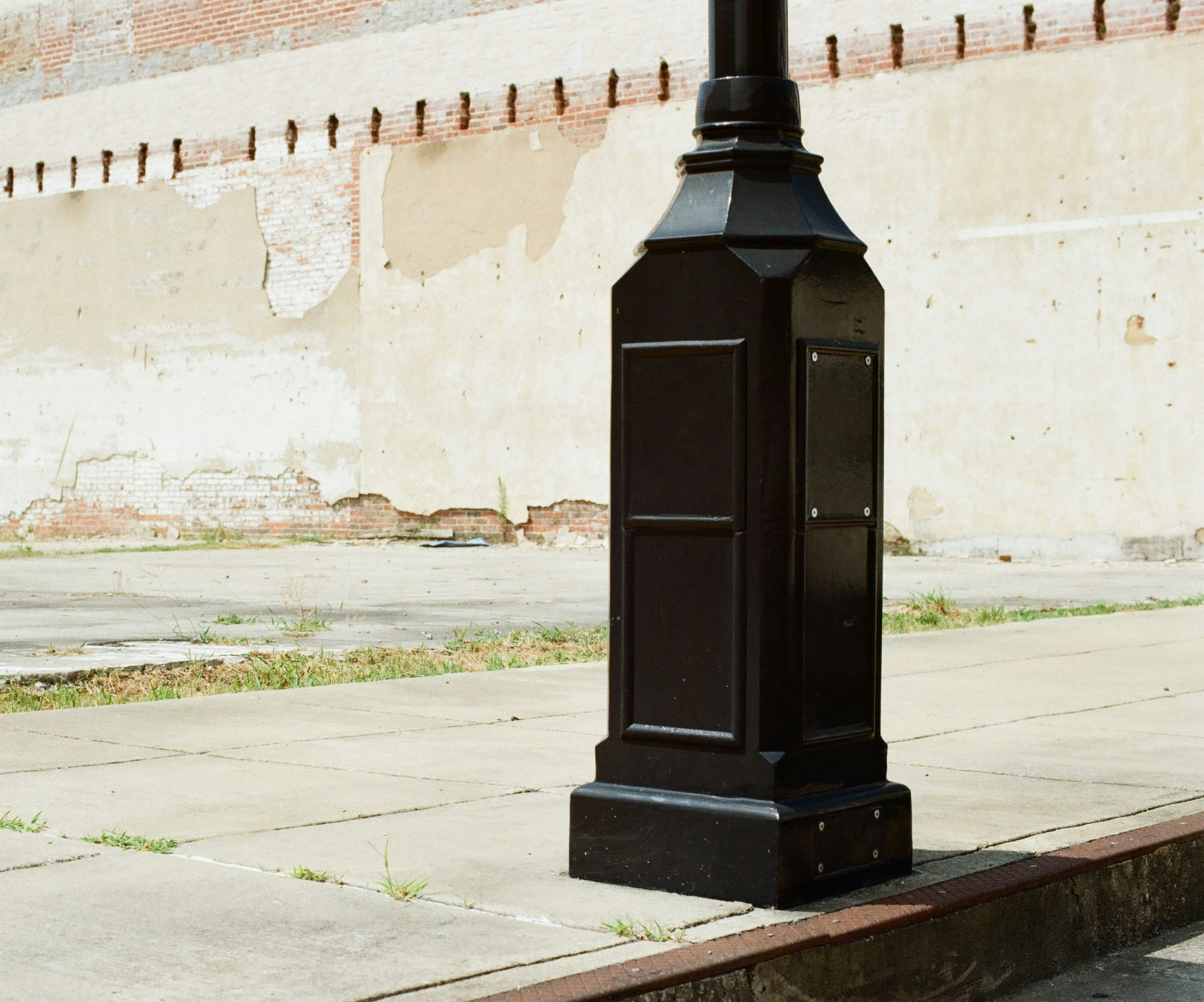 Black street lamp base on sidewalk against a textured wall.