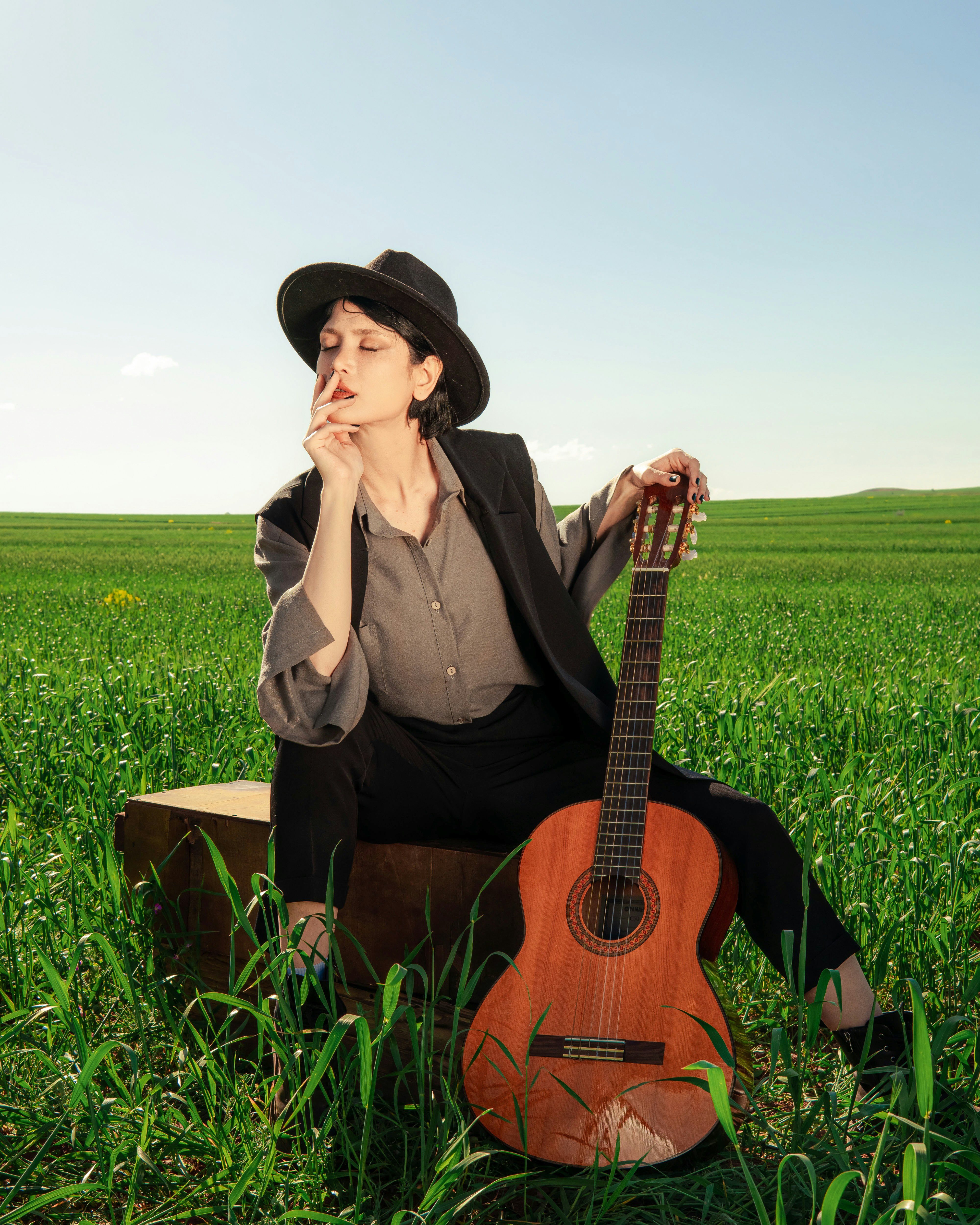 Thoughtful woman with guitar sits on suitcase in green field
