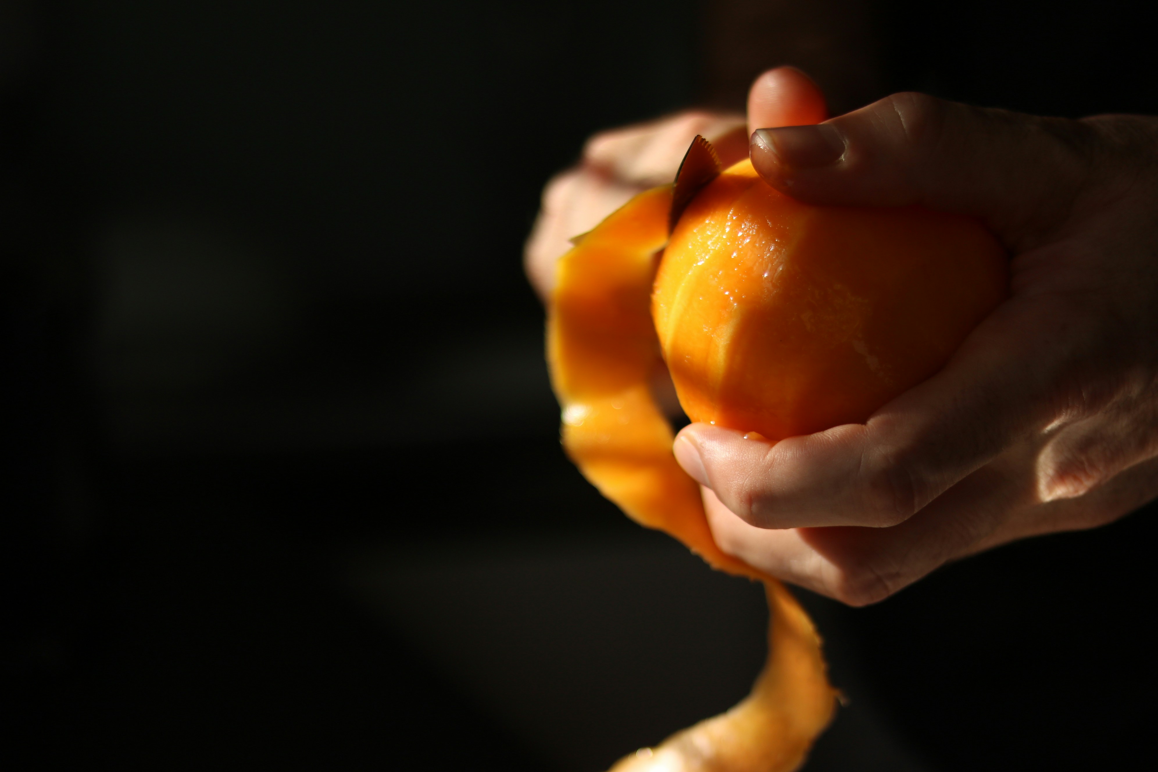 Des mains épluchant une orange fraîche dans une lumière chaude.