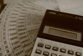A calculator rests on old financial ledger sheets with numbers.