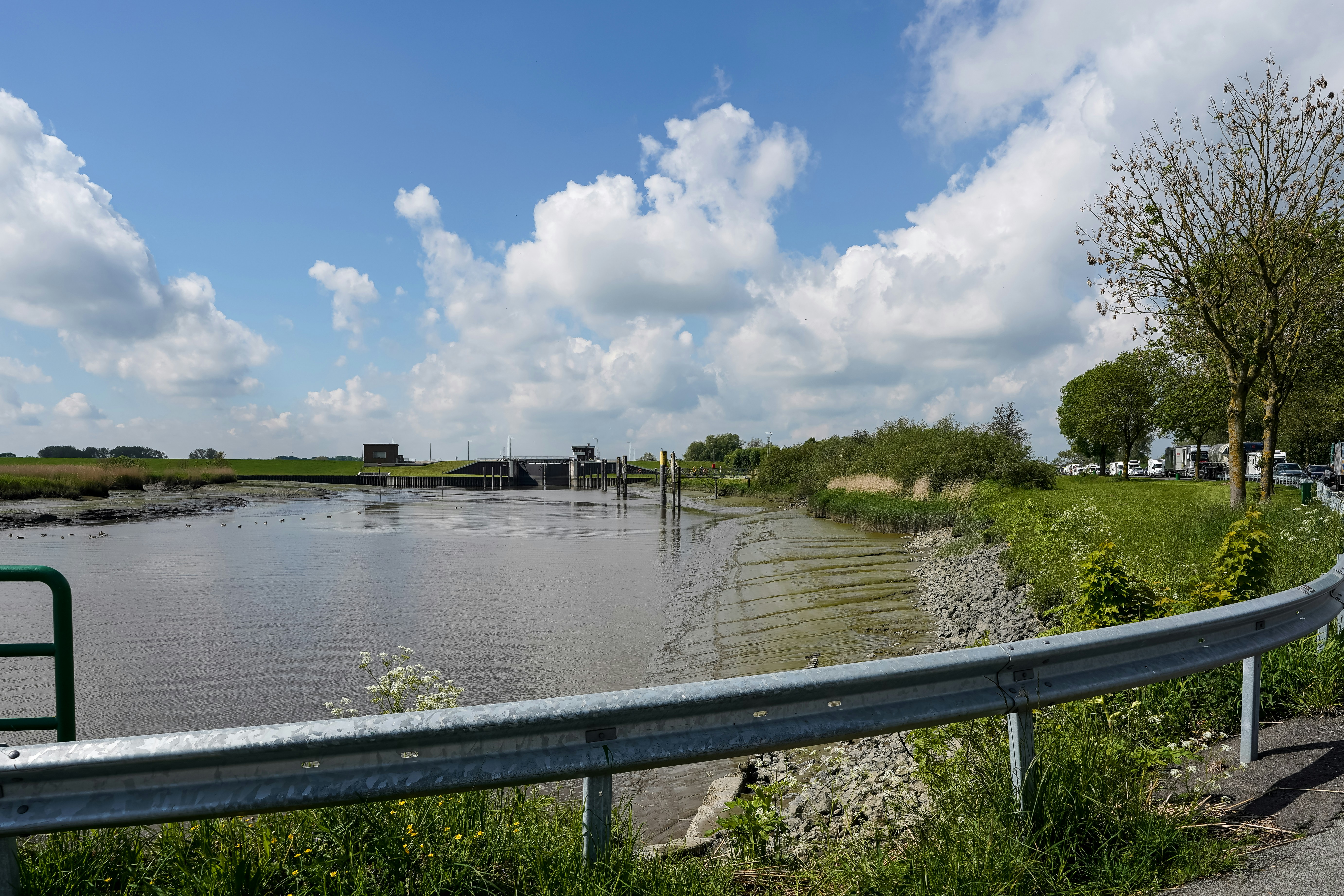 A canal with a guardrail under a cloudy blue sky.