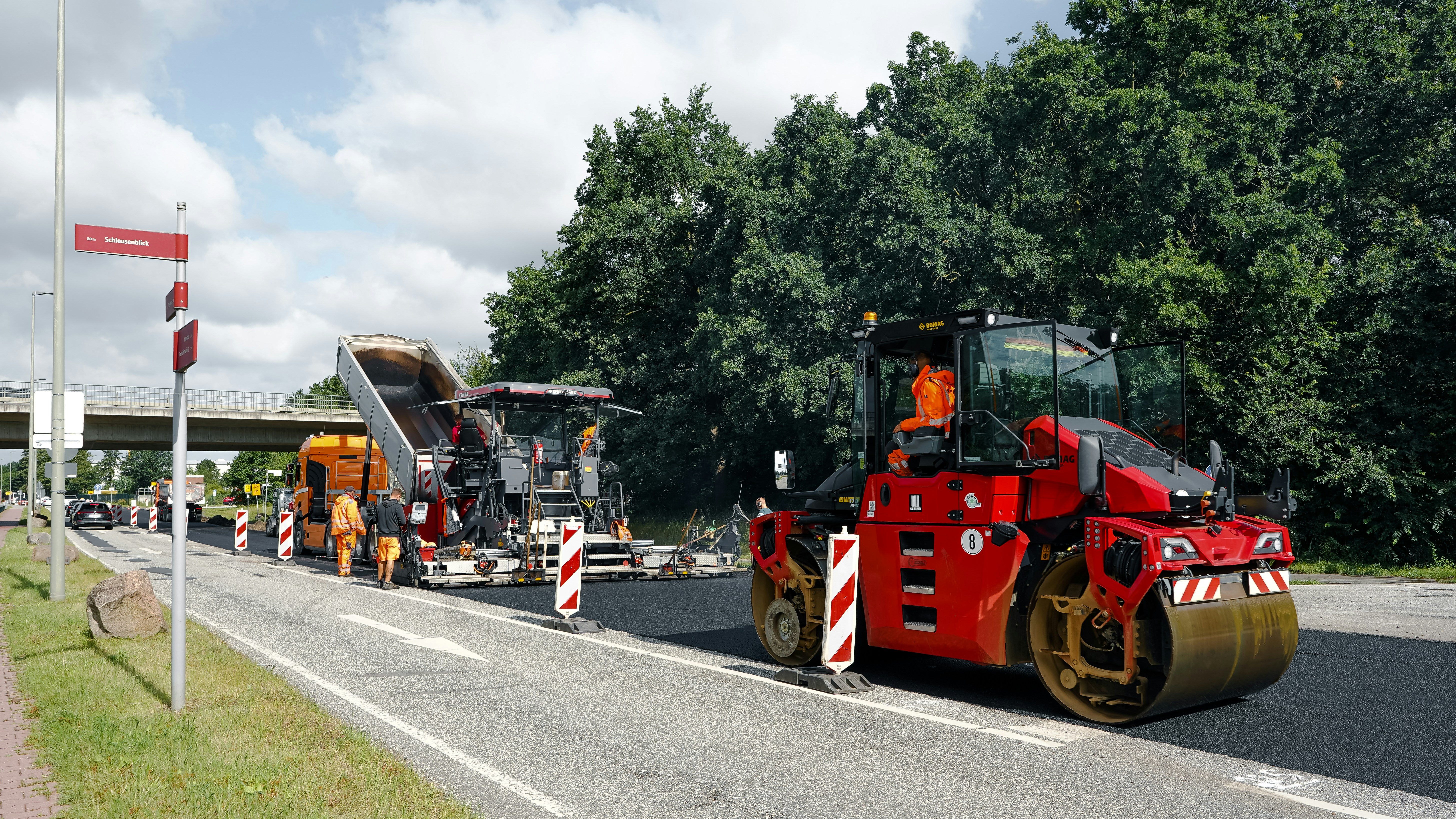Road construction with a red roller and asphalt paver.
