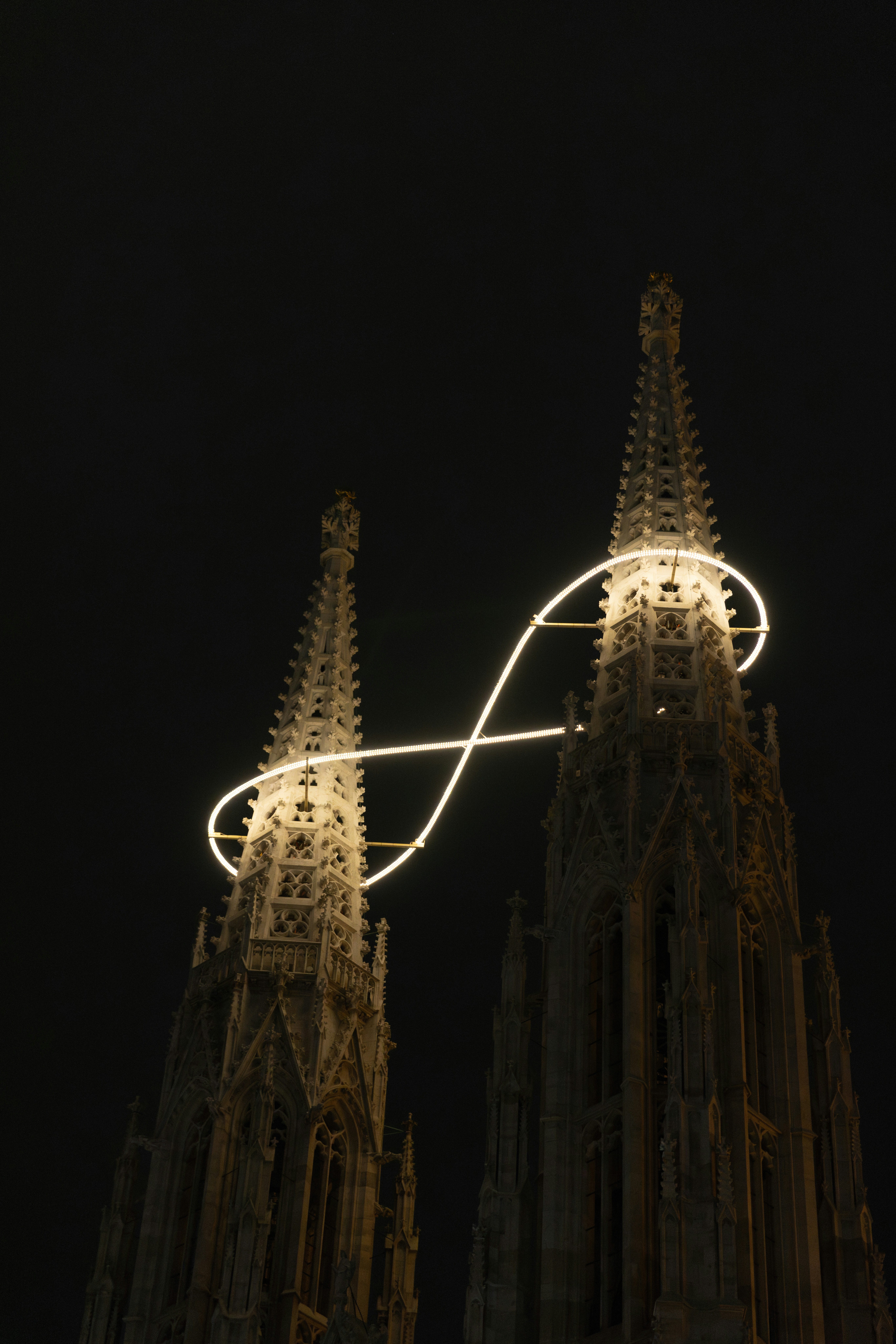 Two church spires illuminated by an infinity symbol at night.