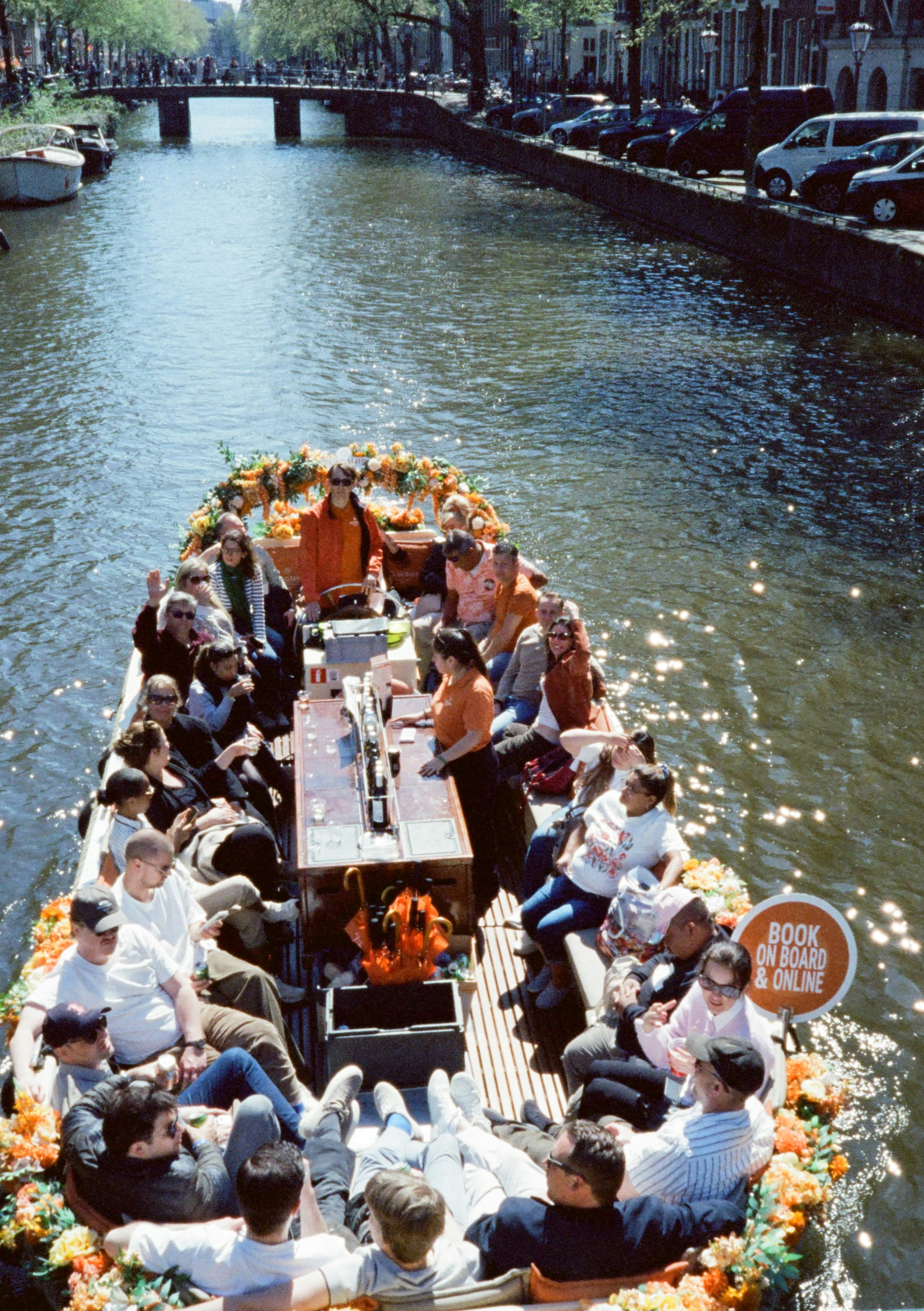 People on an orange flower-decorated boat cruising a city canal