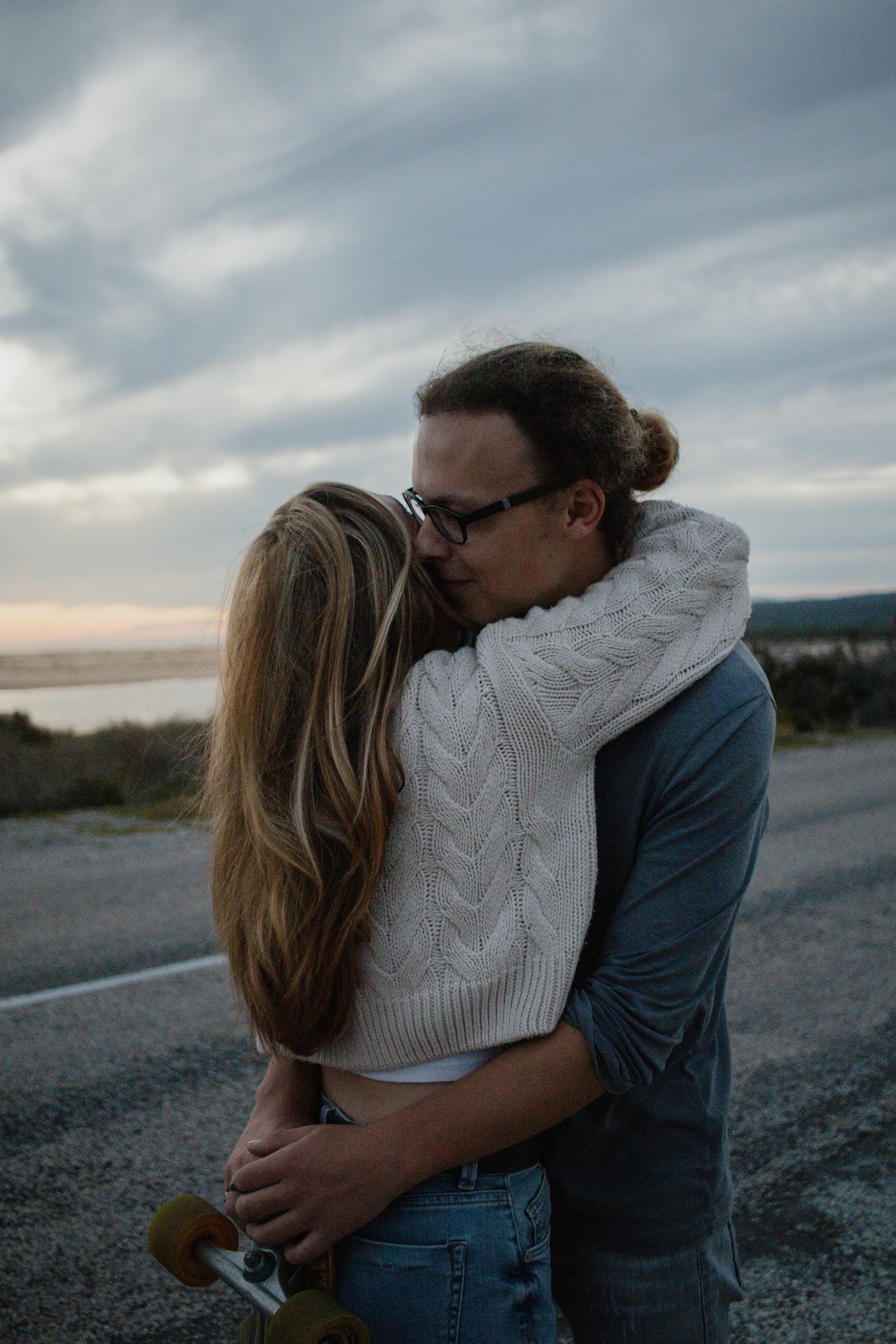 A couple hugging outdoors with a skateboard