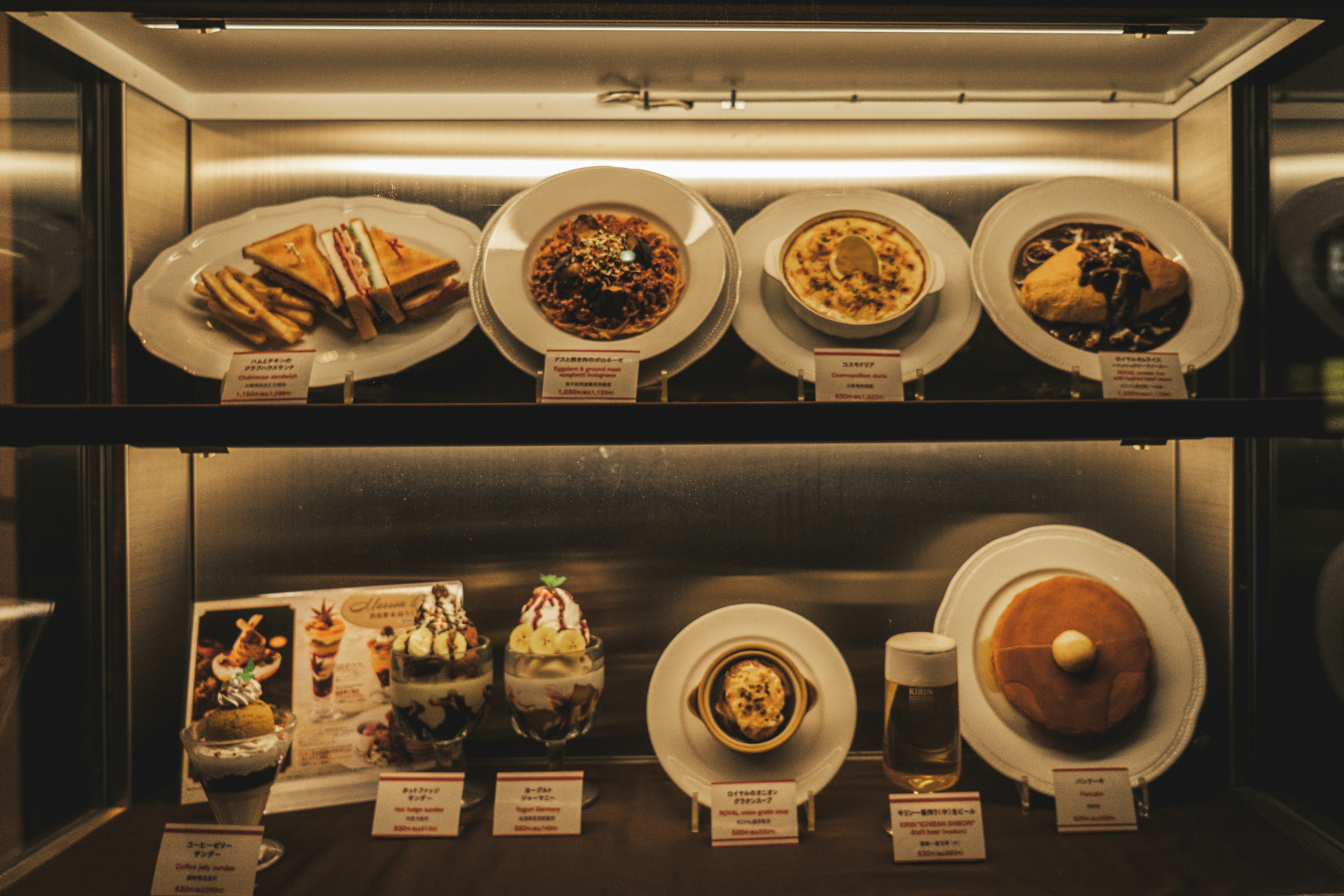 Des modèles culinaires réalistes exposés dans une vitrine de restaurant très éclairée.