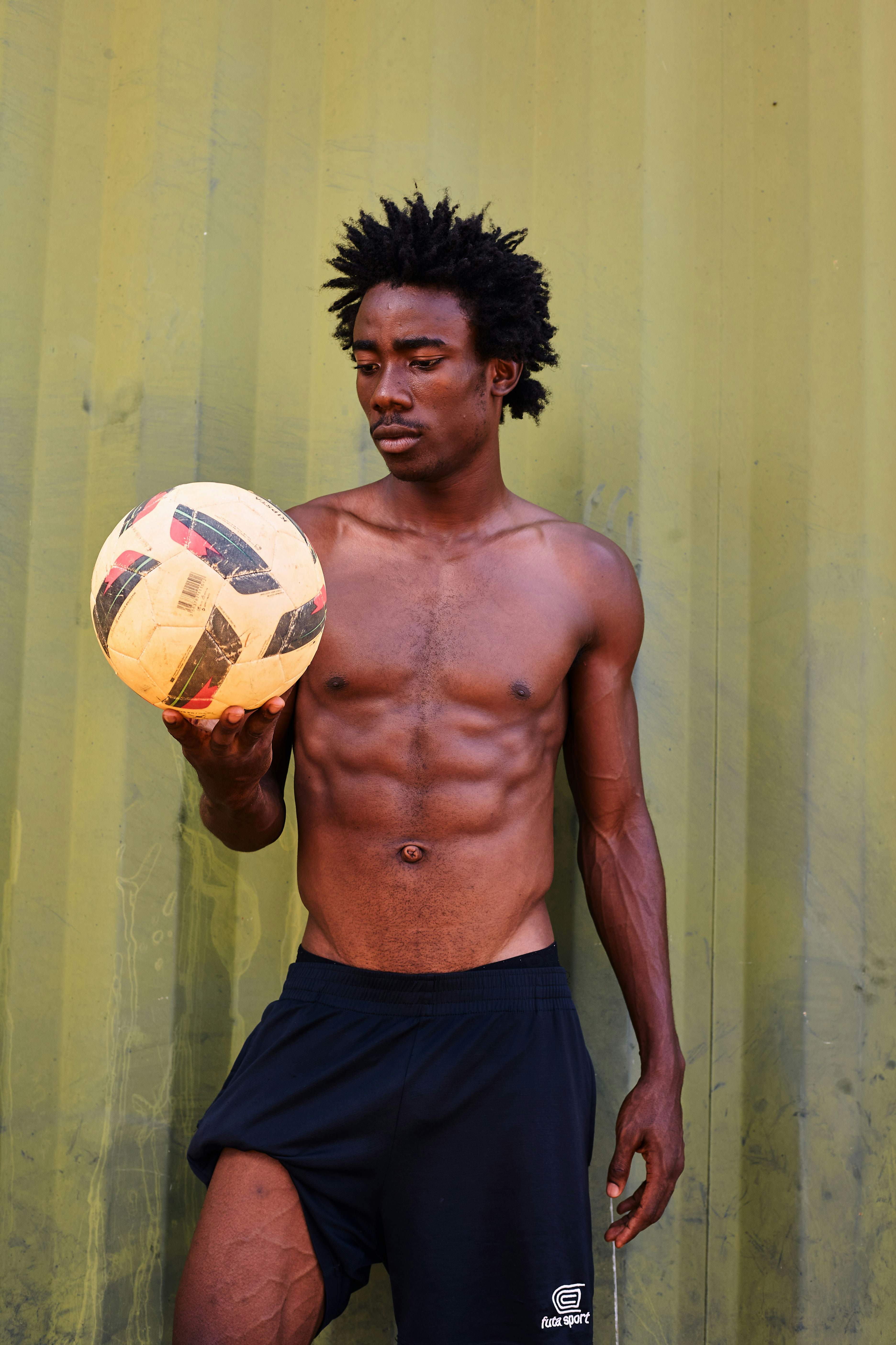 Shirtless man with curly hair holding a soccer ball