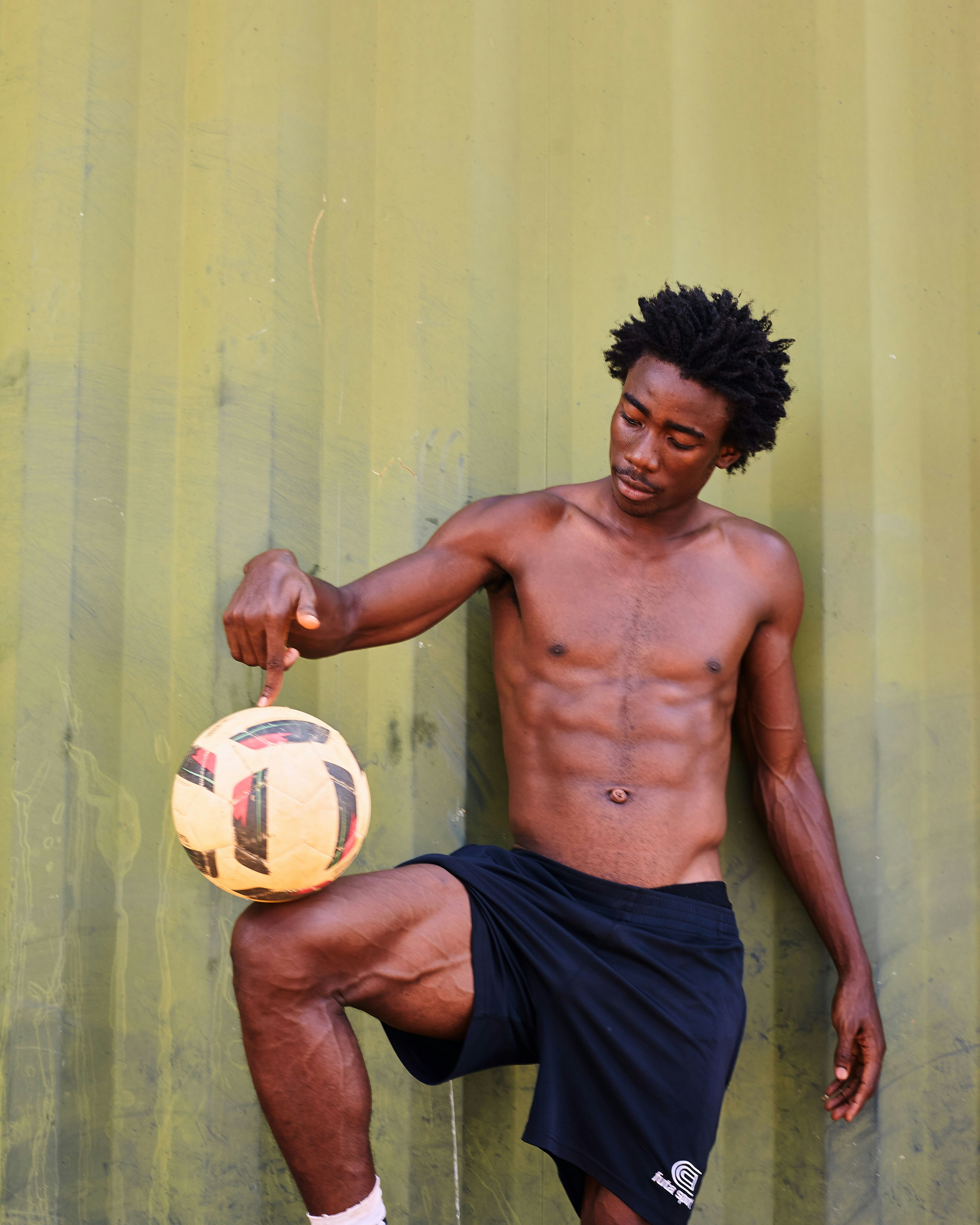 A shirtless man balancing a soccer ball on his finger