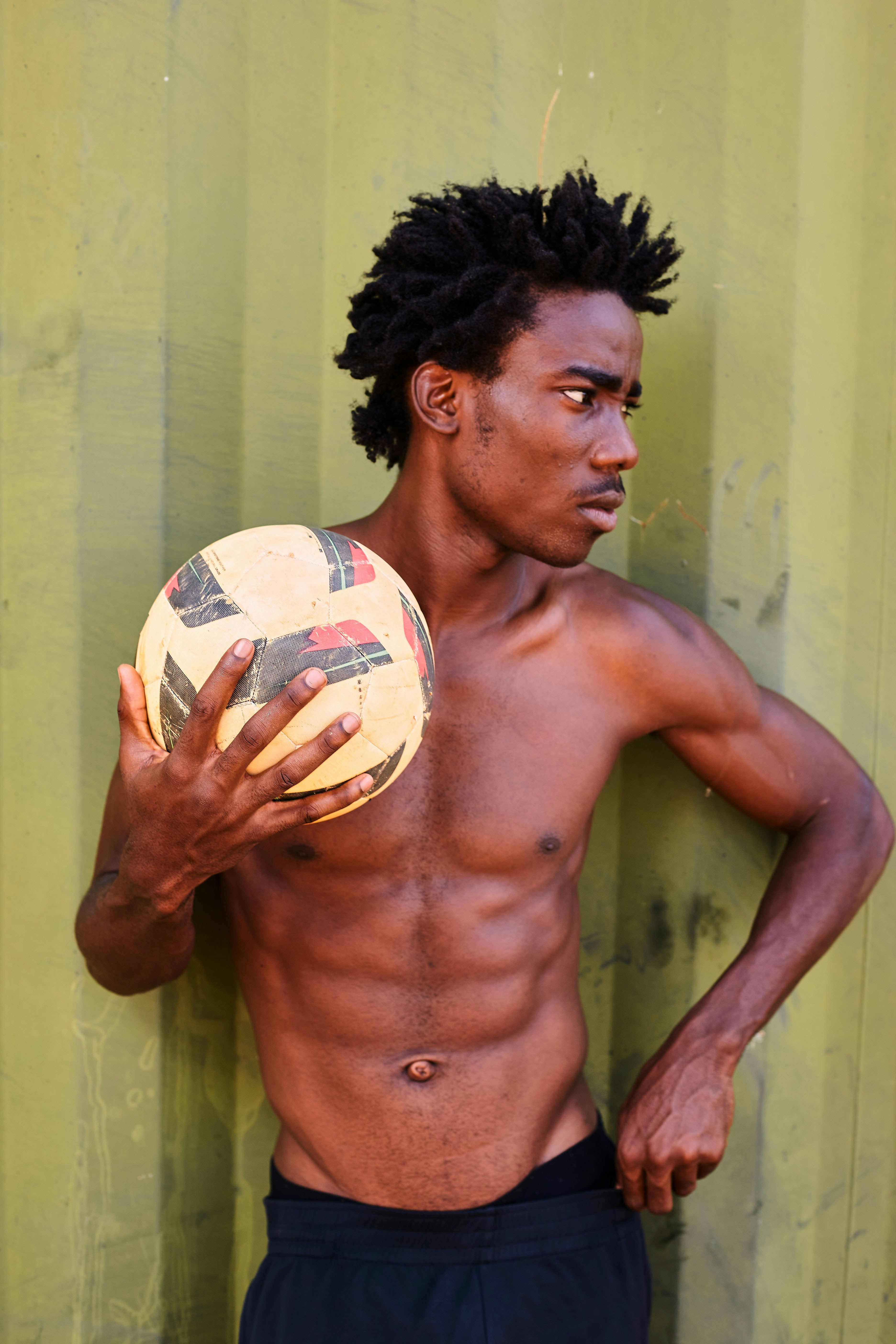 Shirtless man holds soccer ball, looking sideways