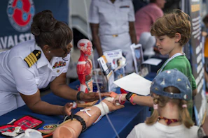 Naval officer demonstrates medical training to curious children.