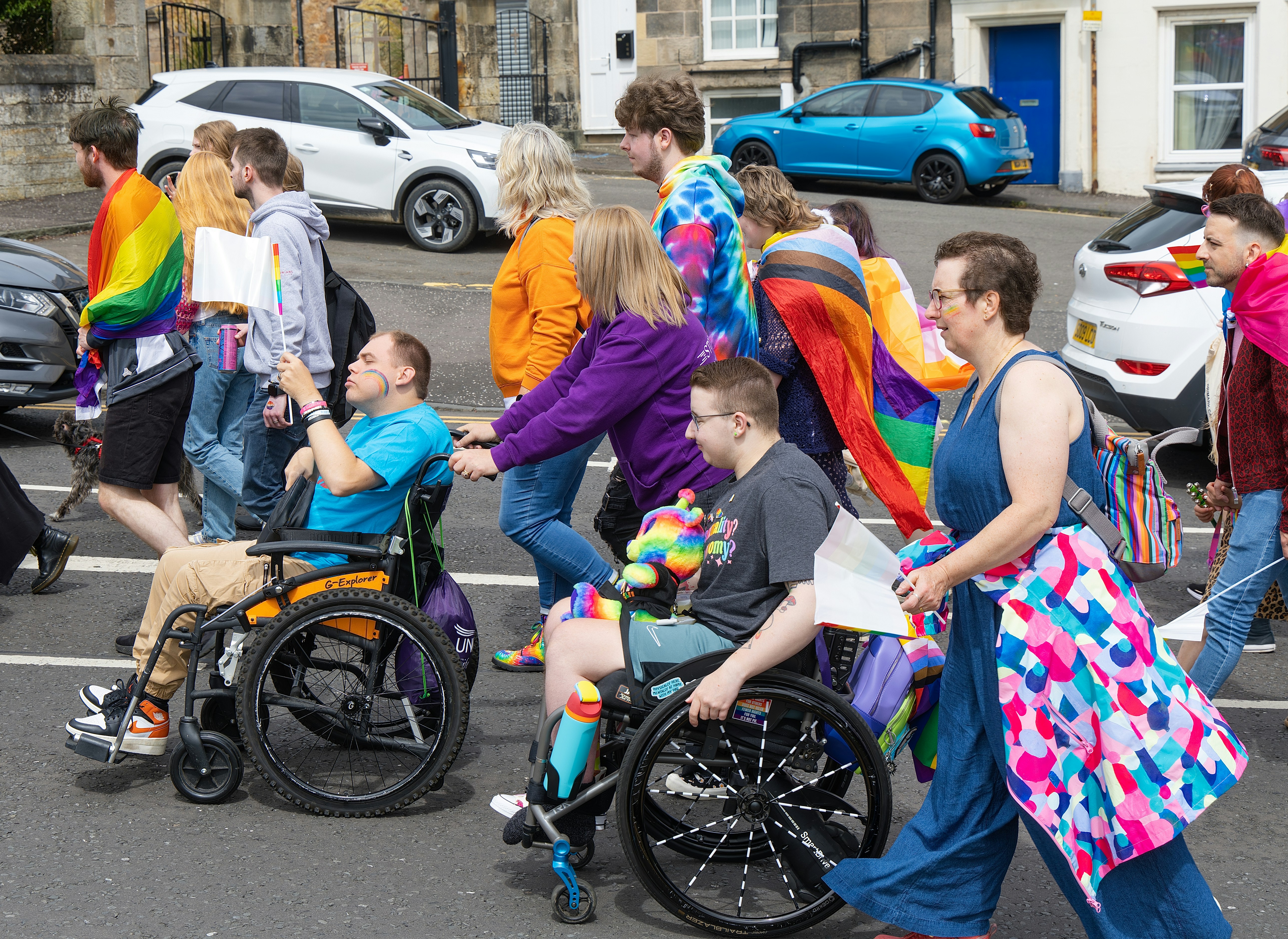 Diverse group, including wheelchair users, at a vibrant pride parade.