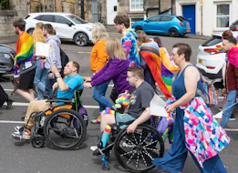 Diverse group, including wheelchair users, at a vibrant pride parade.