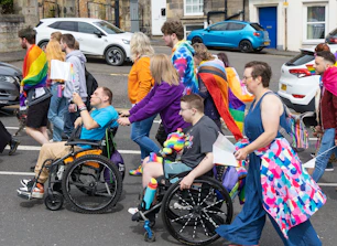 Diverse group, including wheelchair users, at a vibrant pride parade.