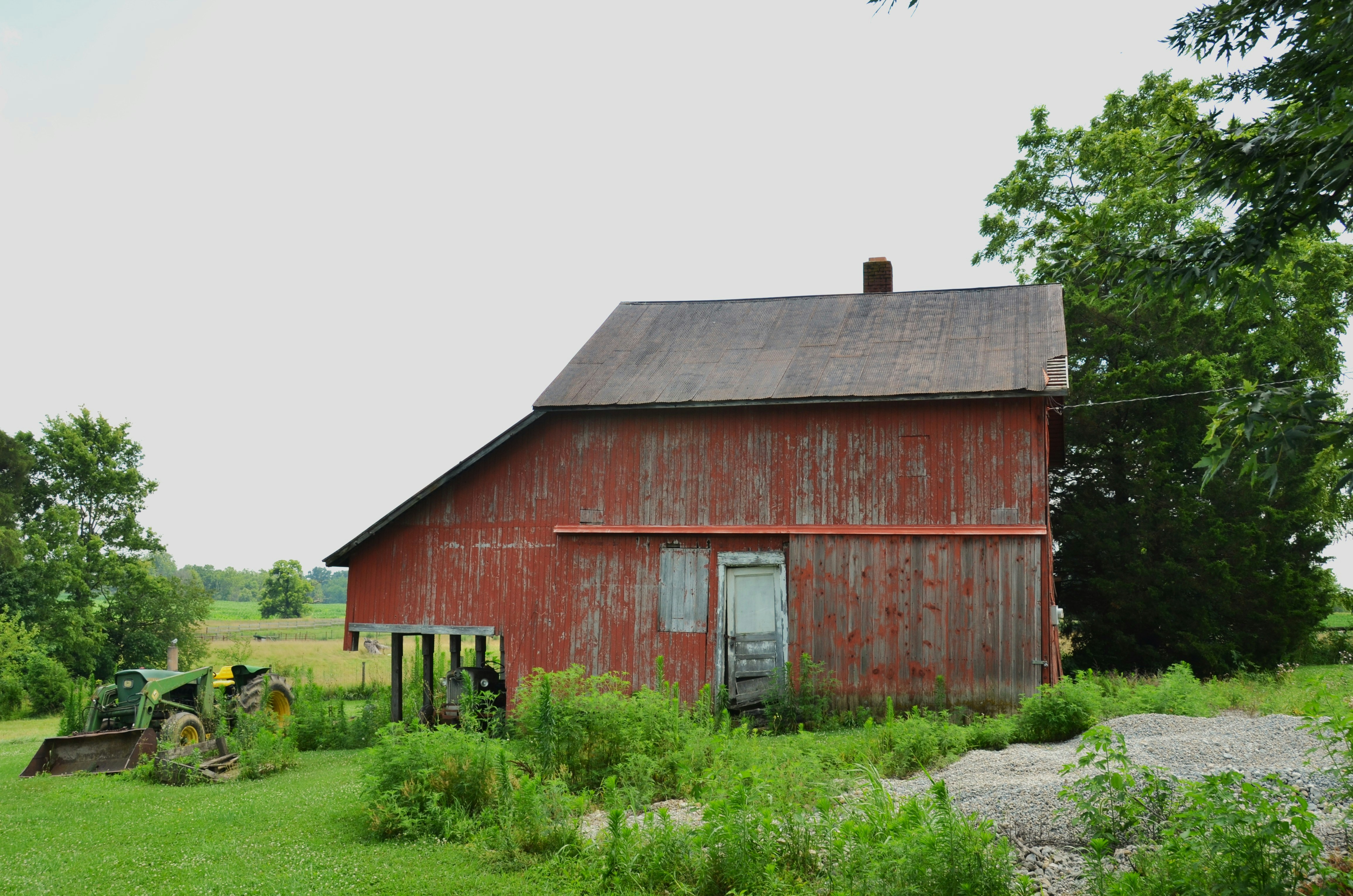 Rustic red barn and tractor in a lush green field.
