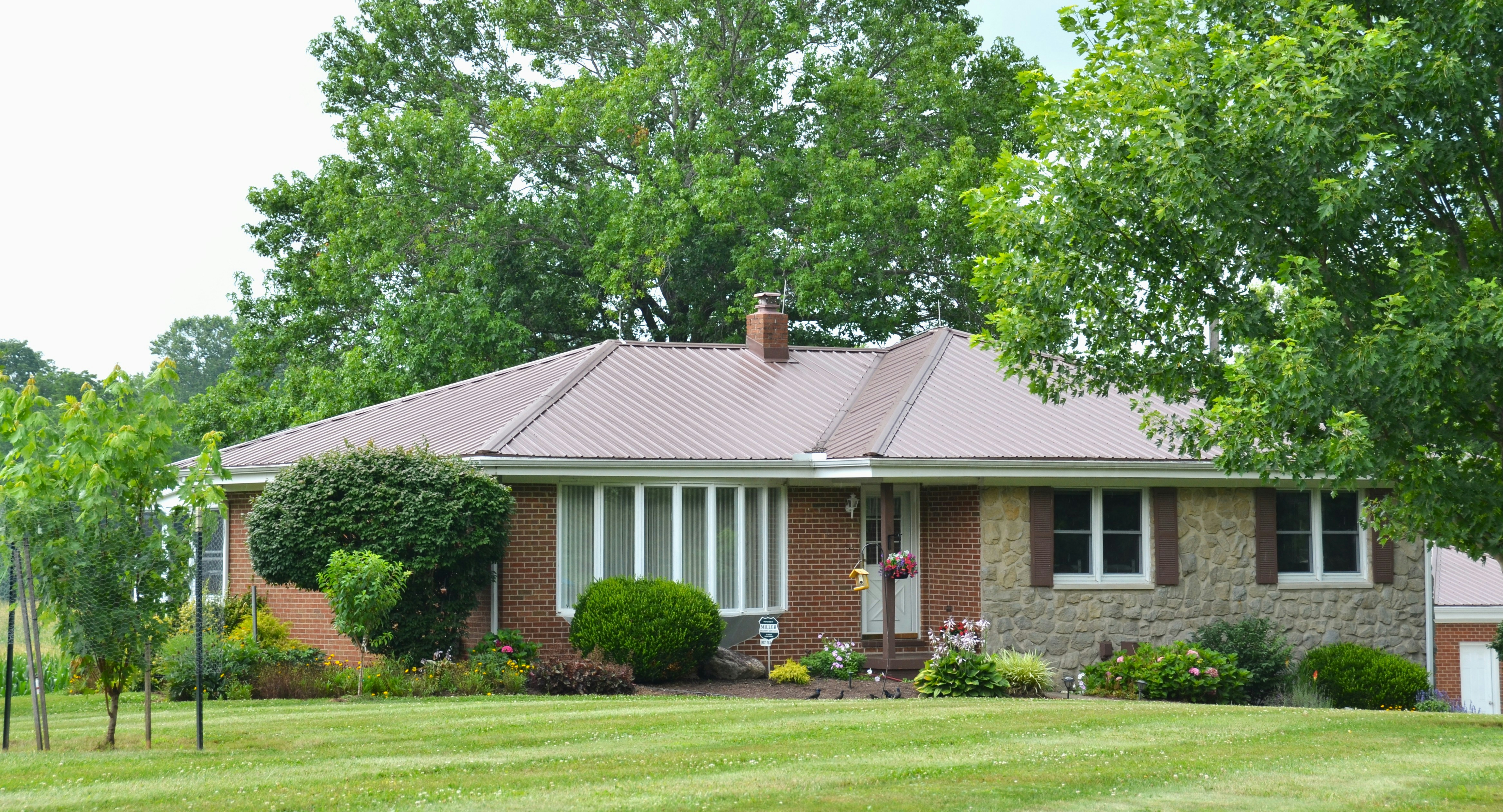 Brick and stone house with brown roof and green trees.