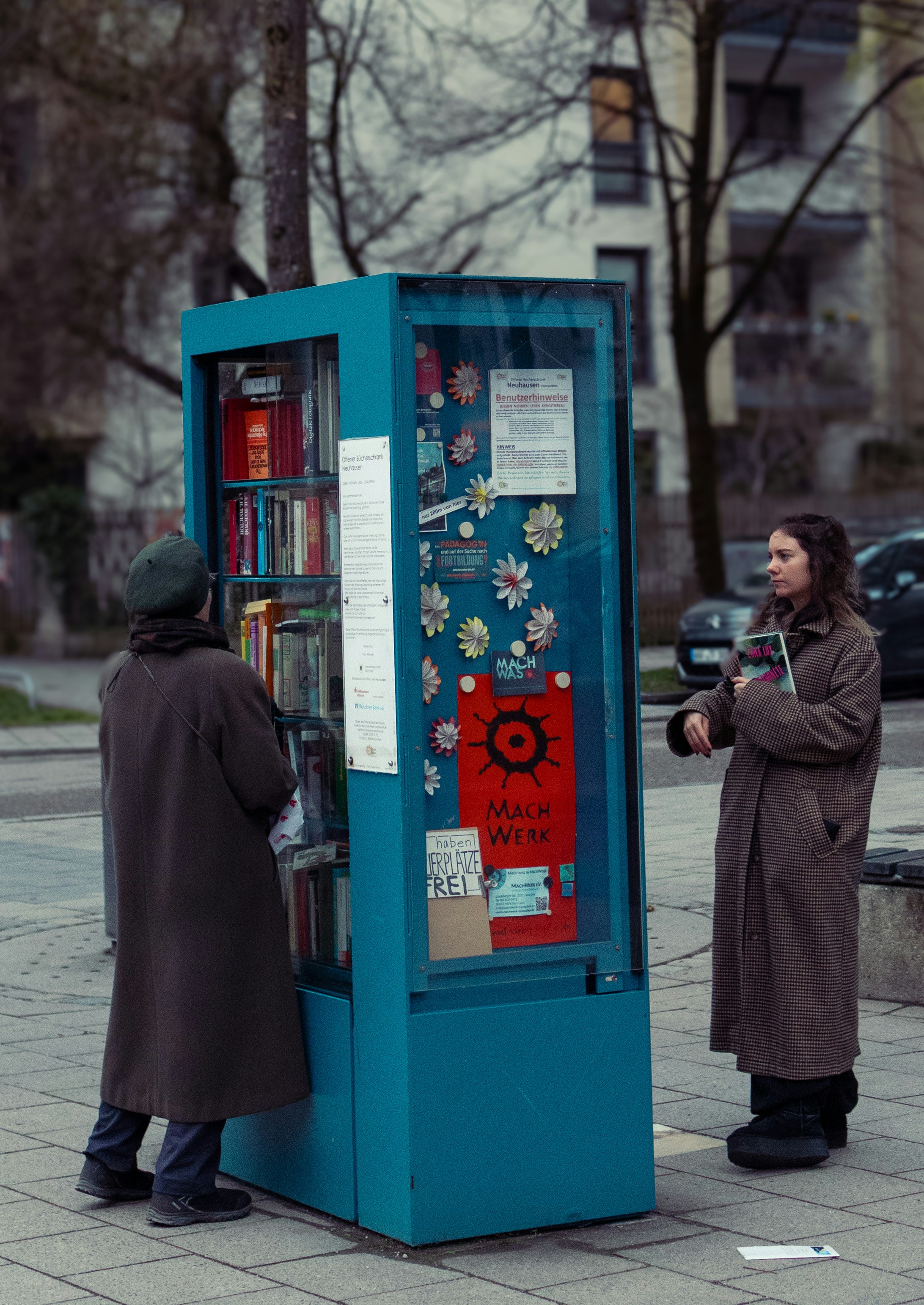 Dos personas hojean libros en una estantería pública azul
