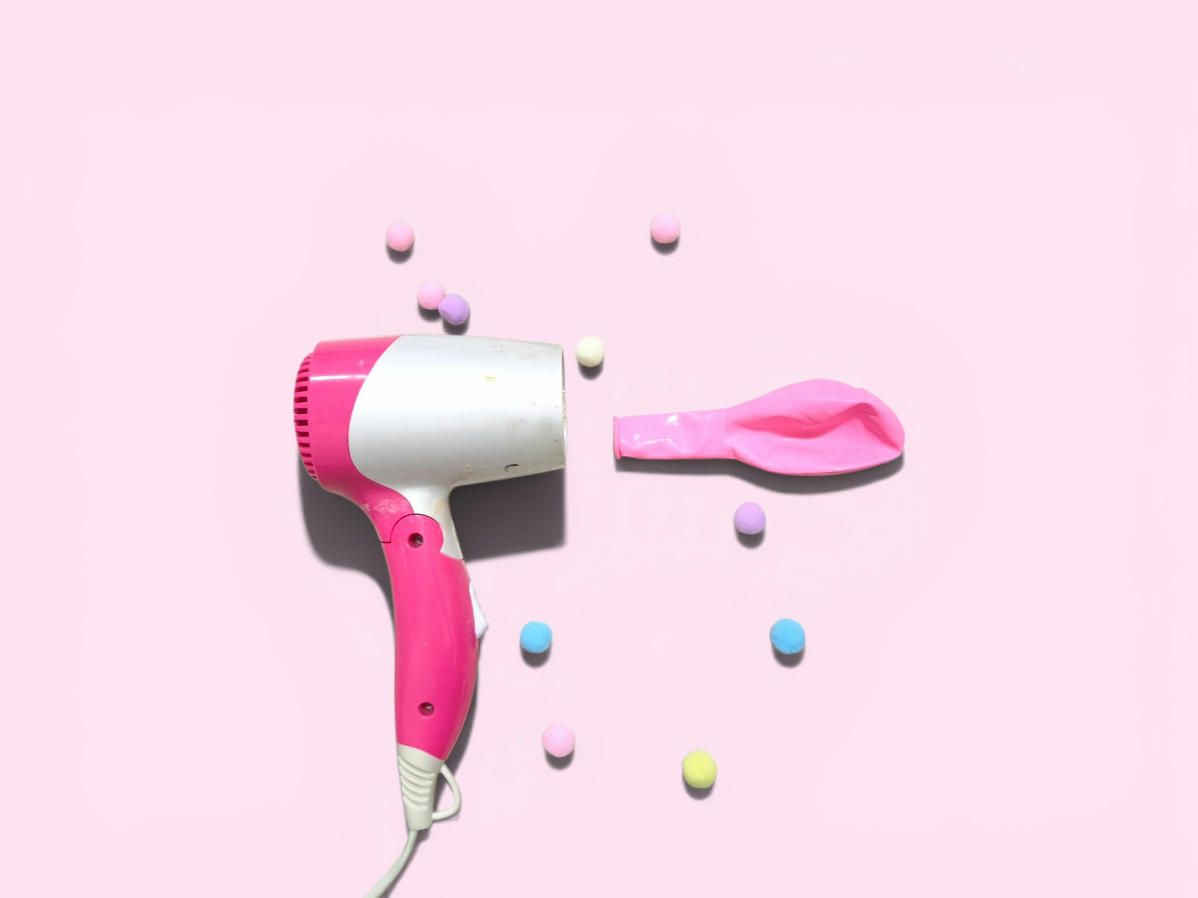 Secador de pelo rosa, globo desinflado y caramelos coloridos sobre fondo rosa