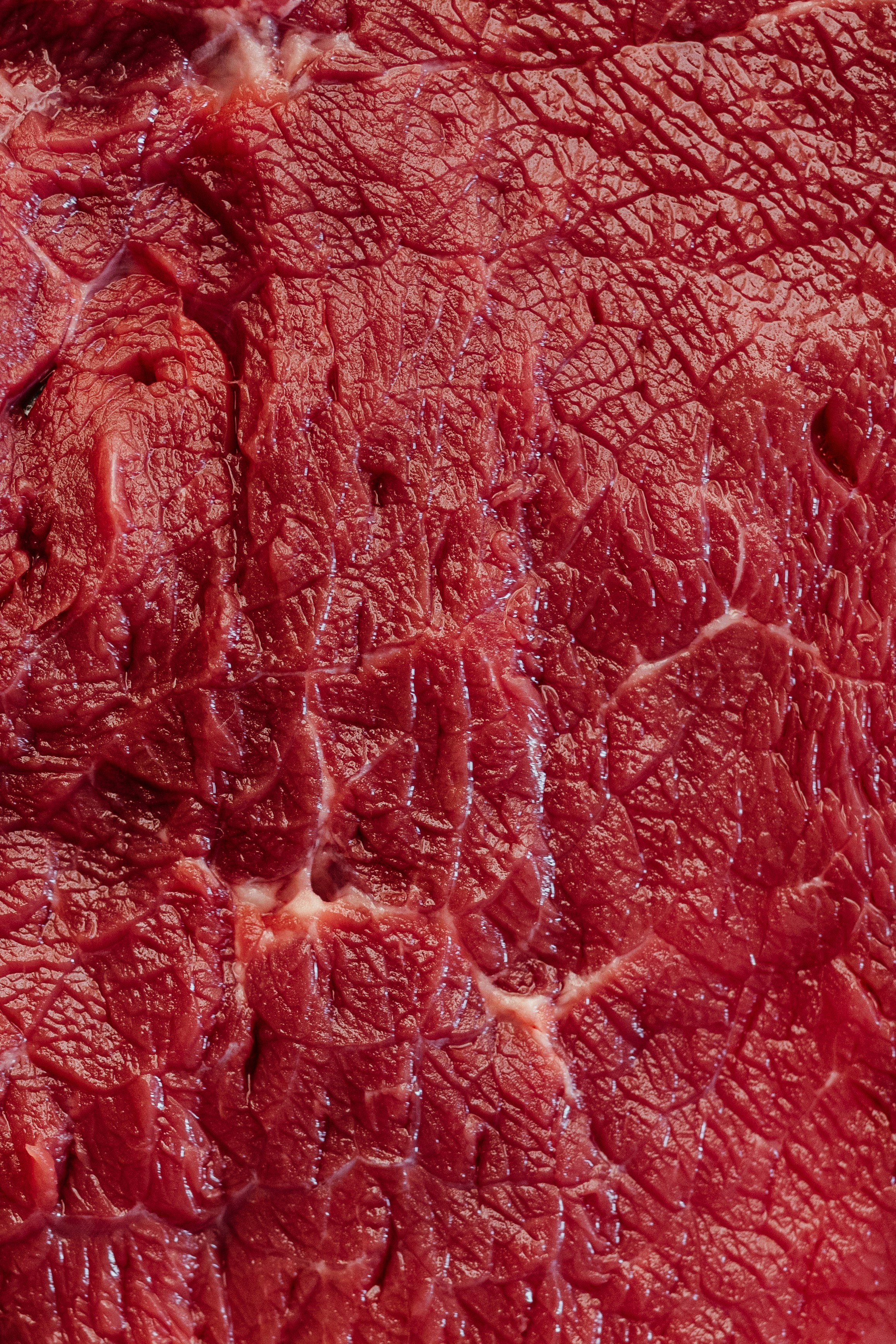 Textured surface of raw, vibrant red meat.