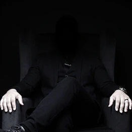 Mysterious man in dark suit sits in a chair.