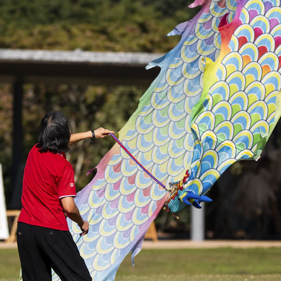 A person holds a large, colorful dragon kite outdoors.