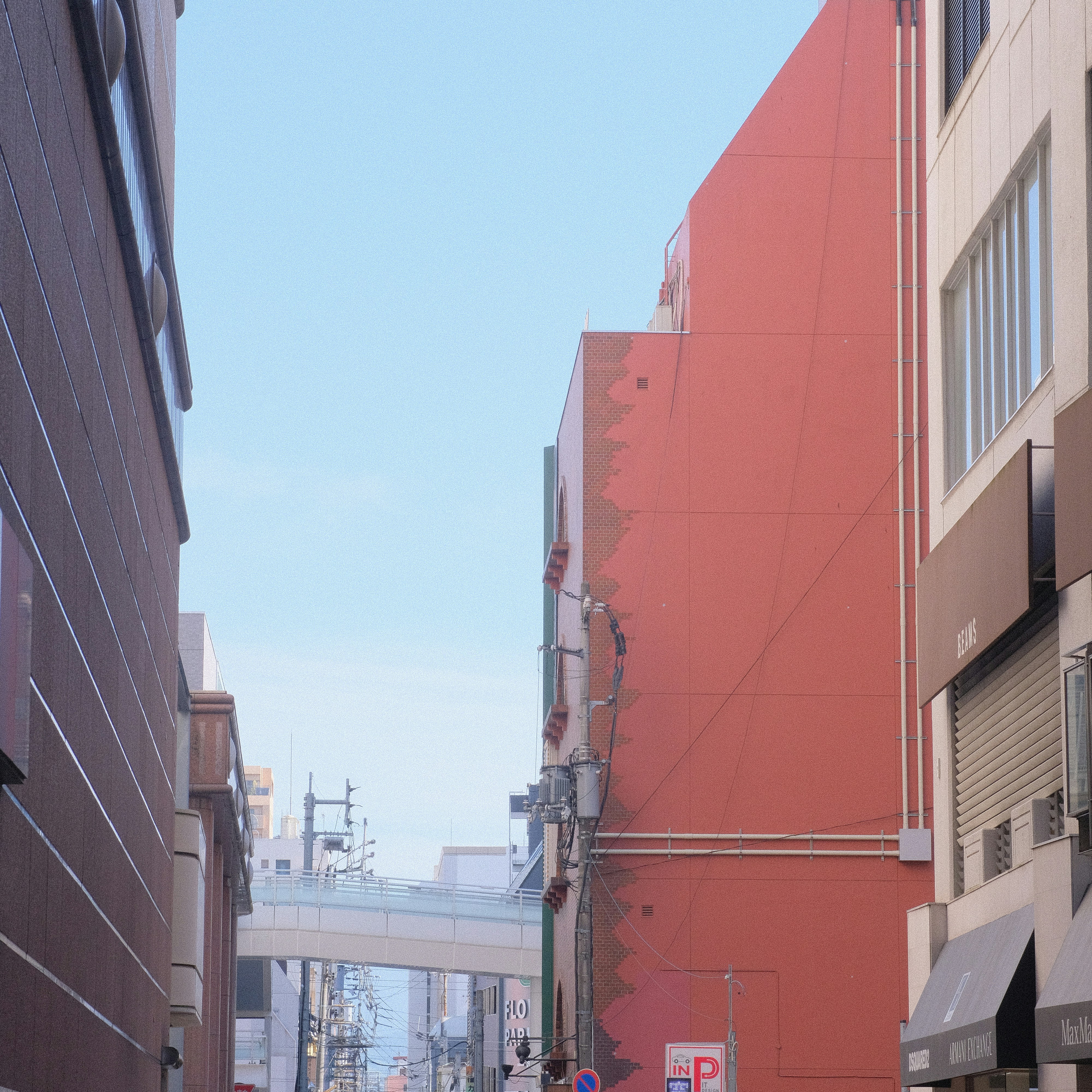 Rua estreita com prédio vermelho, céu azul e ponte distante.