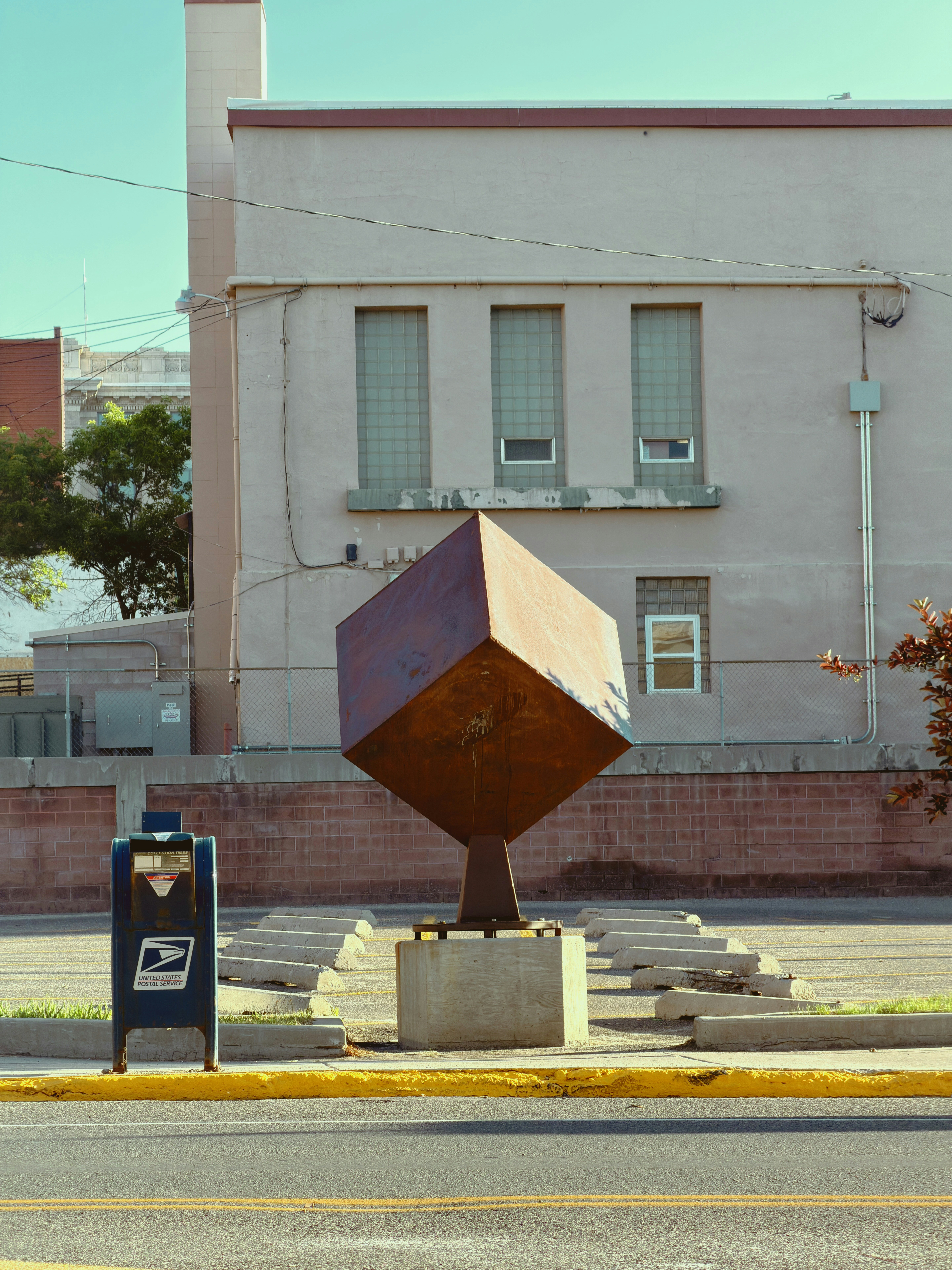 Rusty geometric sculpture and mailbox on an urban street.
