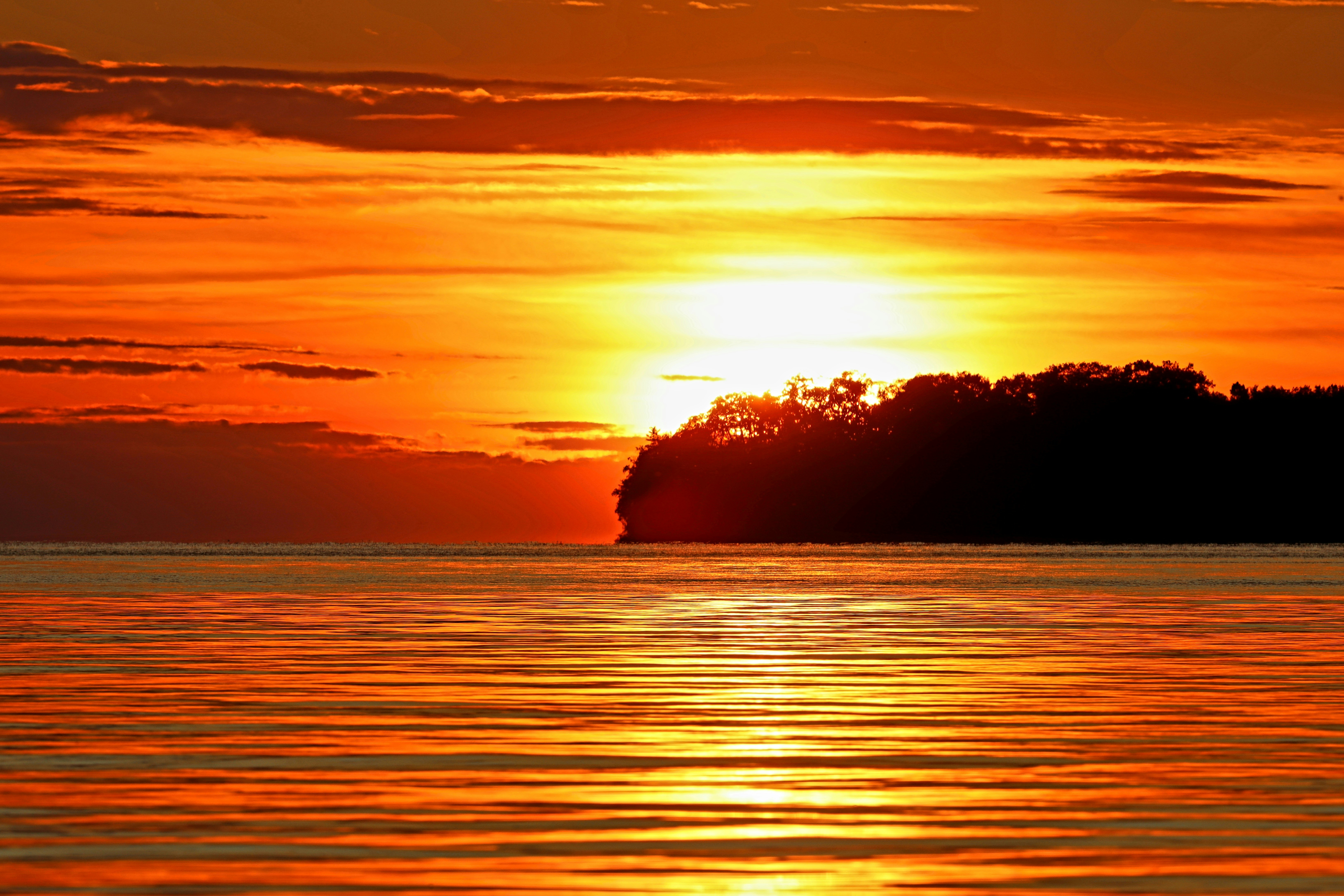 Matahari terbenam oranye cerah di atas air dengan pulau siluet.