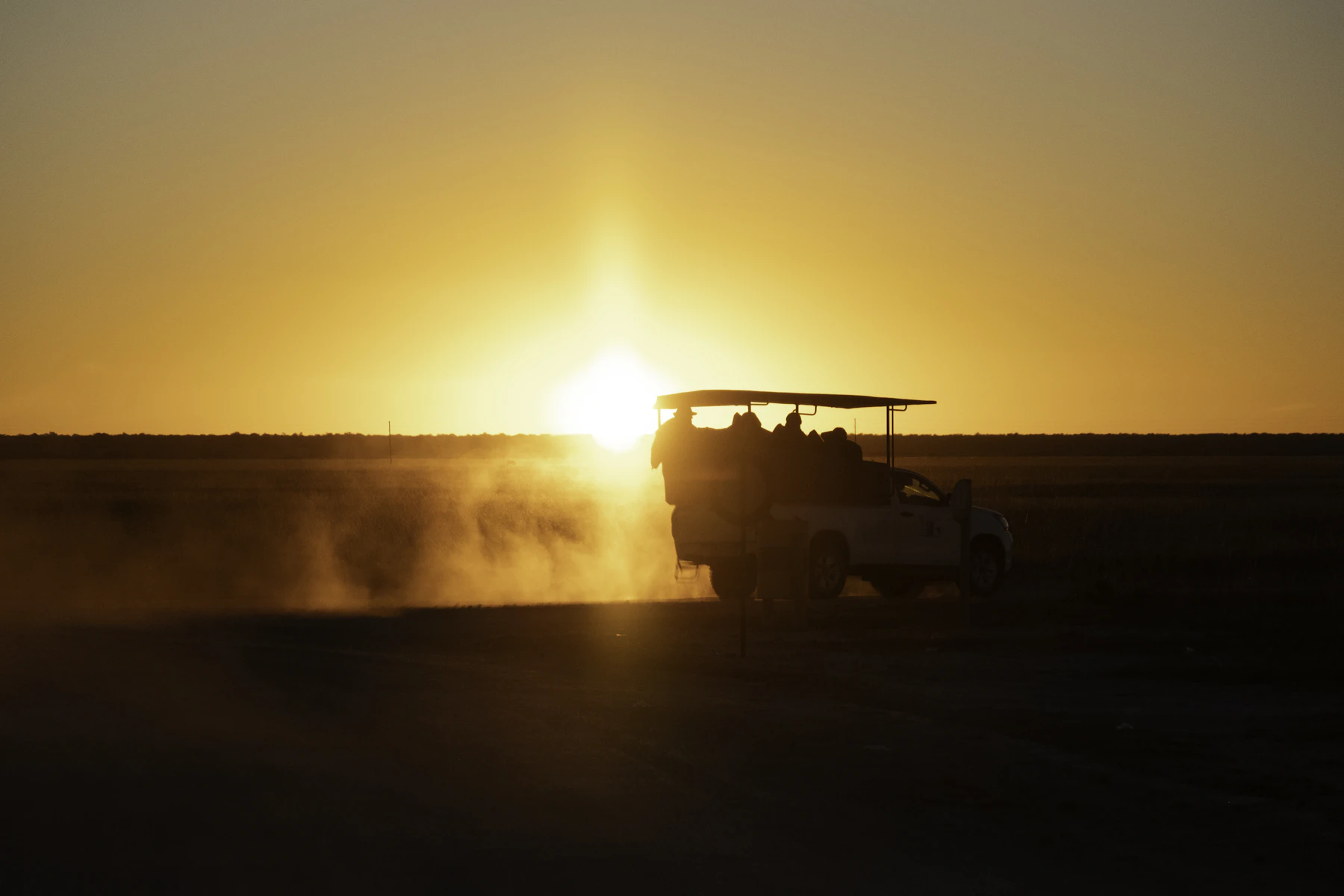 Safari vehicle driving across the Kenyan savannah at sunset, dust rising behind it