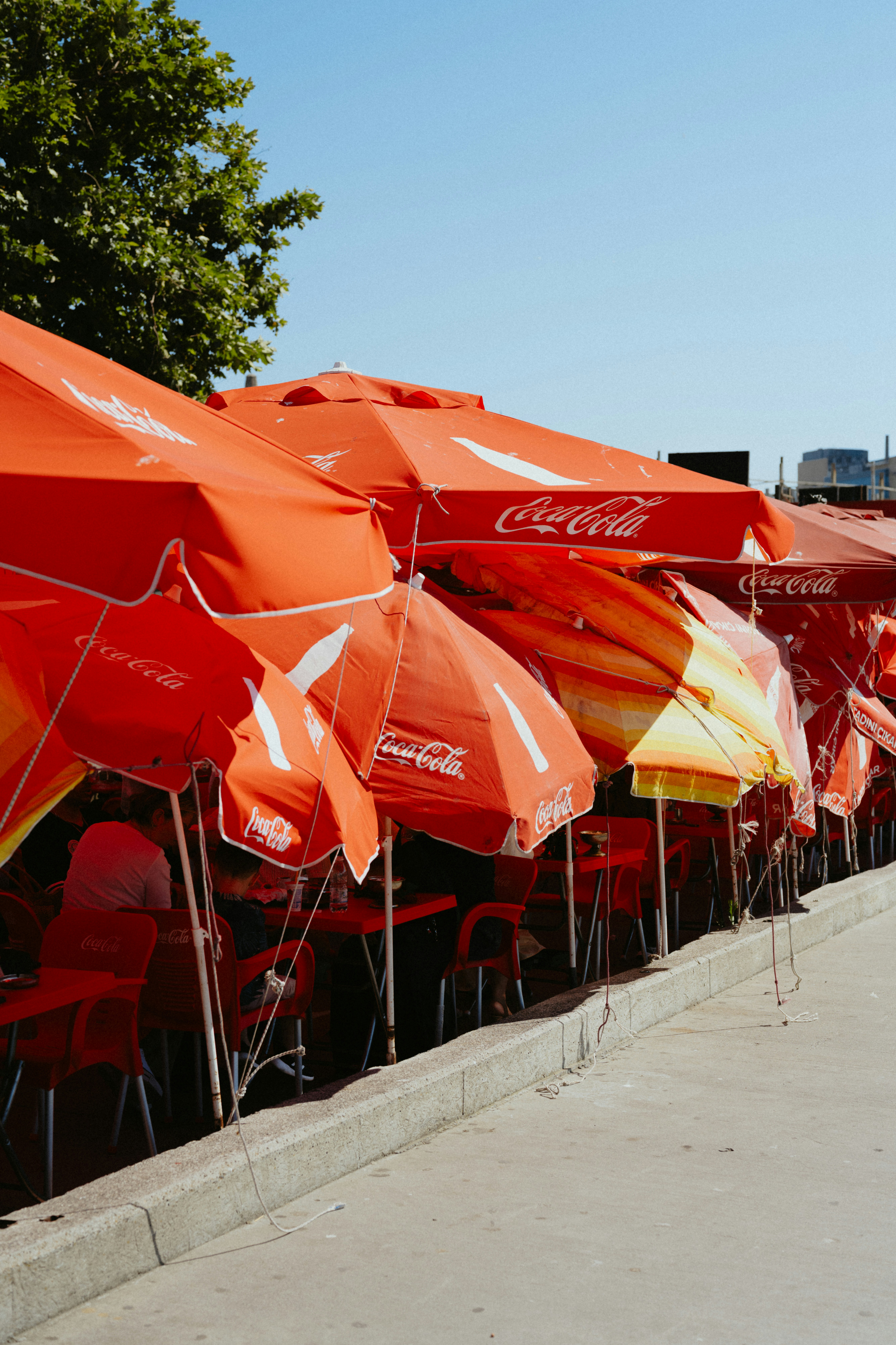 Photo of Red coca-cola umbrellas cover an outdoor seating area. by Tolga Ahmetler