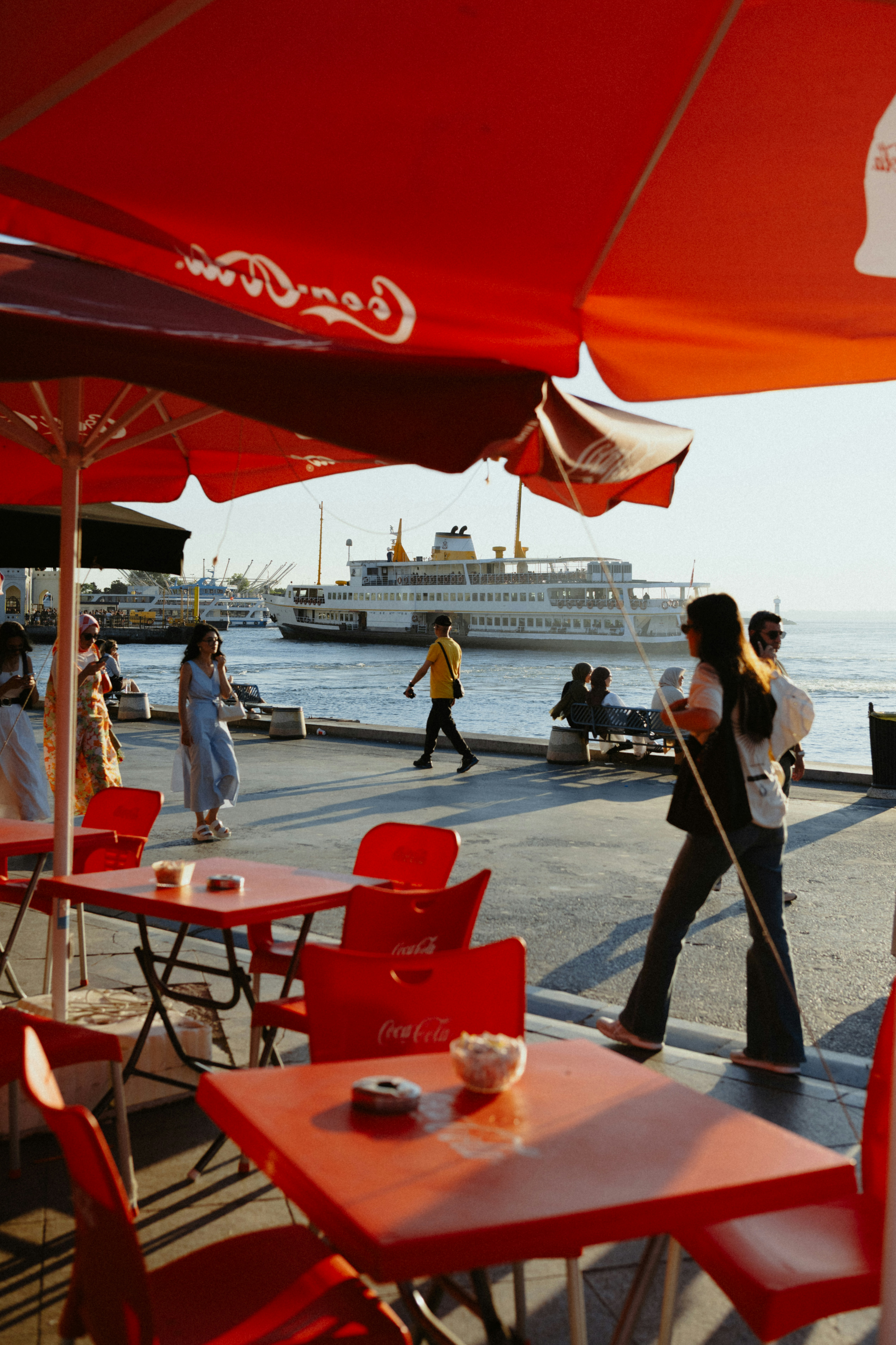 Photo of Red cafe tables by a waterfront with a ferry boat. by Tolga Ahmetler