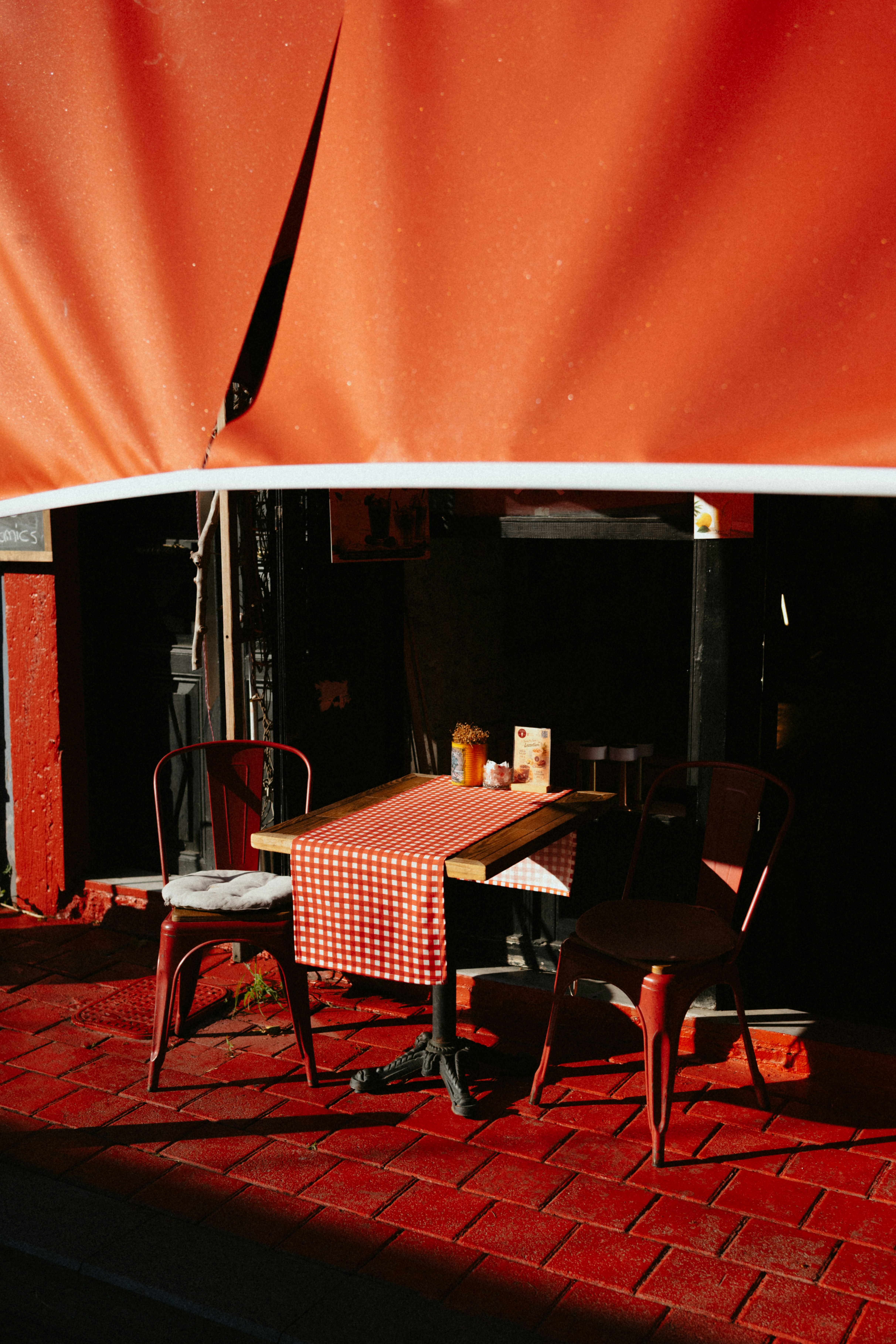 Photo of Outdoor cafe table and chairs under a vibrant red awning. by Tolga Ahmetler
