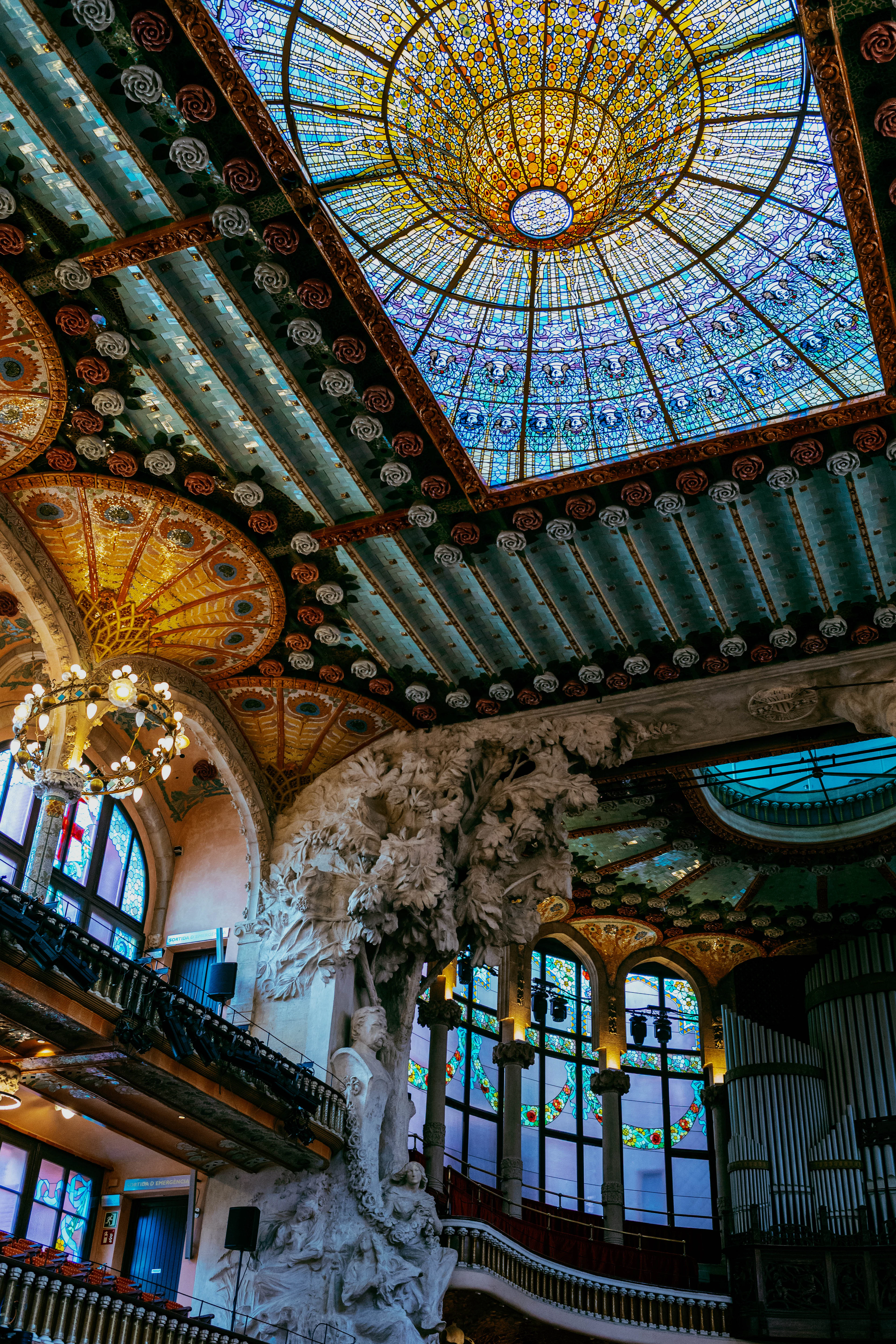 The inverted stained-glass skylight of the Palau de la Musica Catalana in Barcelona blazing gold and blue above the hall's sculpted proscenium and organ pipes.