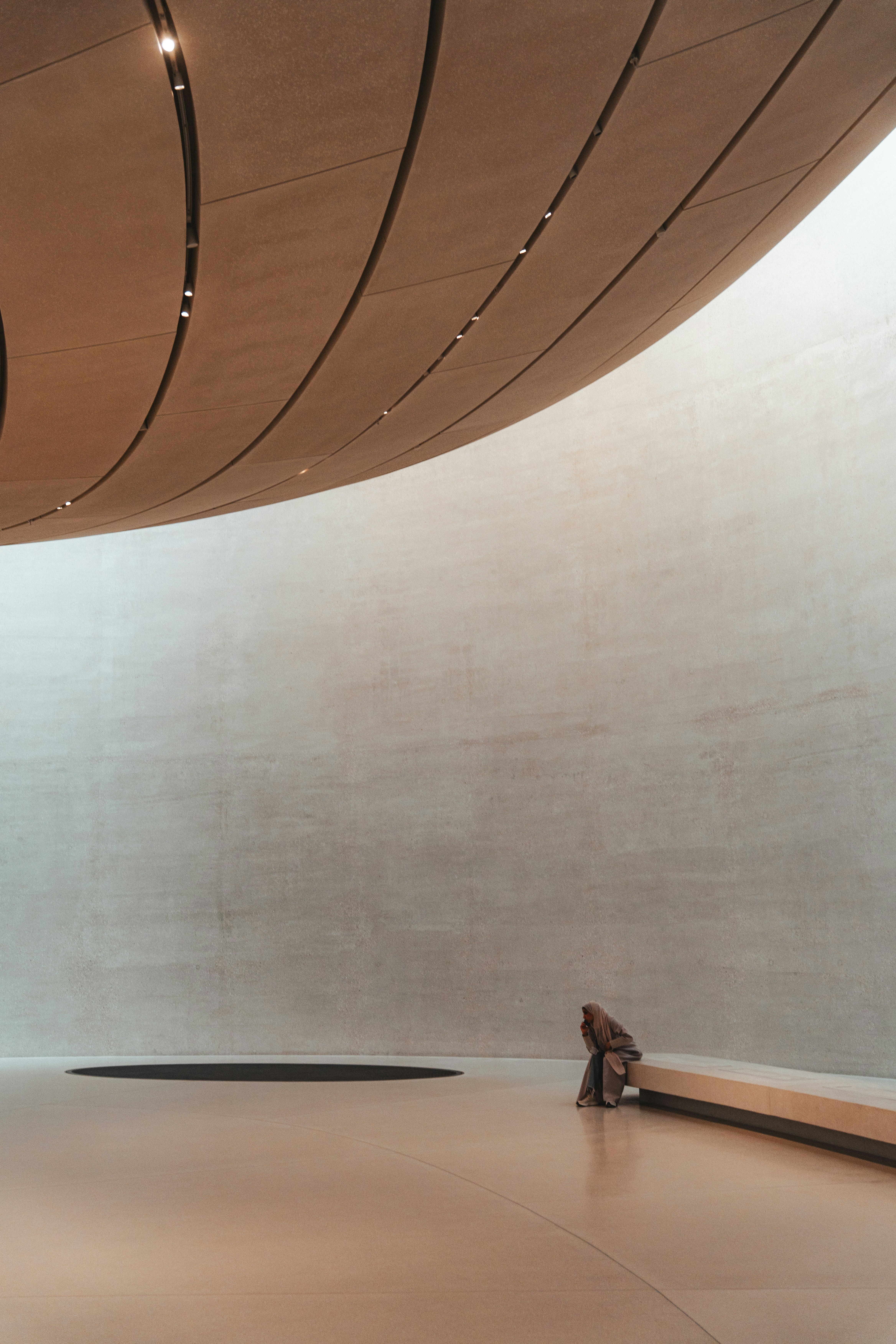 Person sits on a bench in a large, minimalist hall.