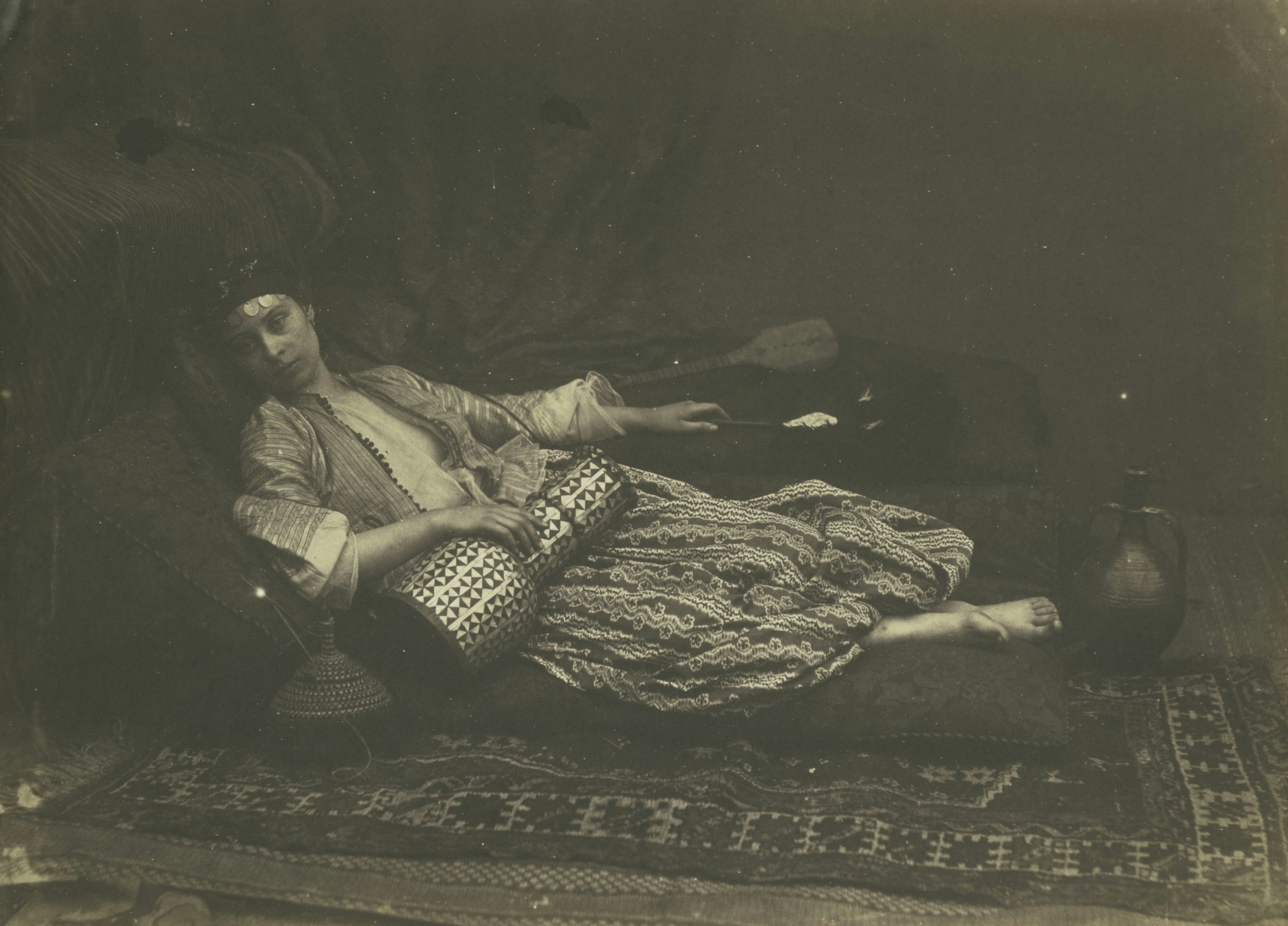 A woman reclines on a patterned rug with a jug