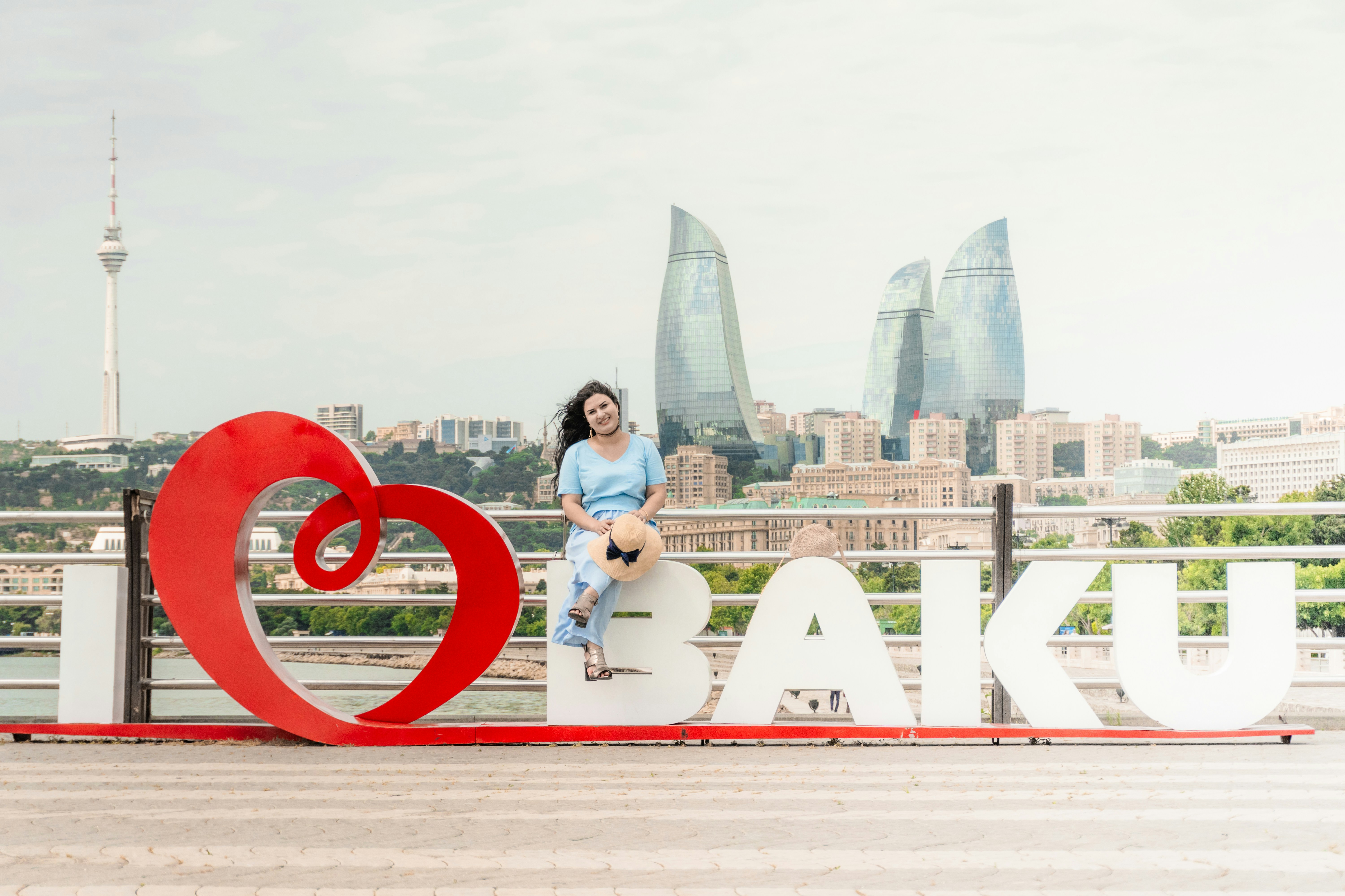 女性が「I love Baku」と「シティスカイライン」の看板に座っている。