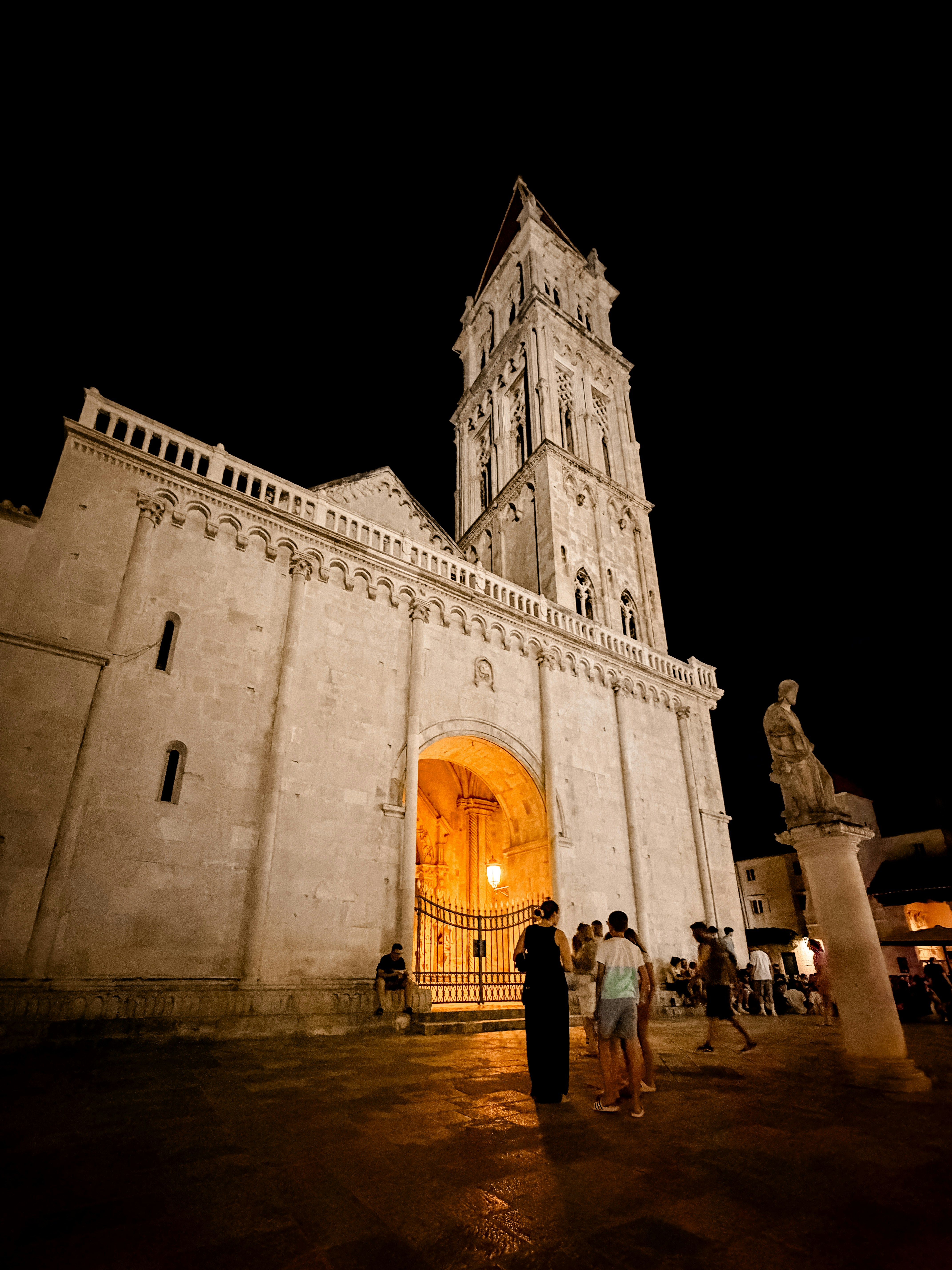Illuminated historic cathedral and bell tower at night with people