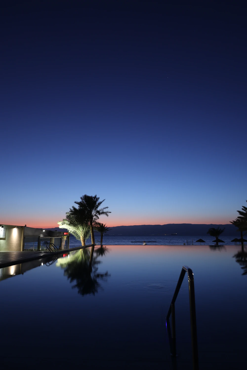 Backyard pool reflecting a warm twilight sky, framed by palm trees