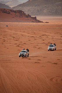 Two white suvs traverse a vast sandy desert landscape